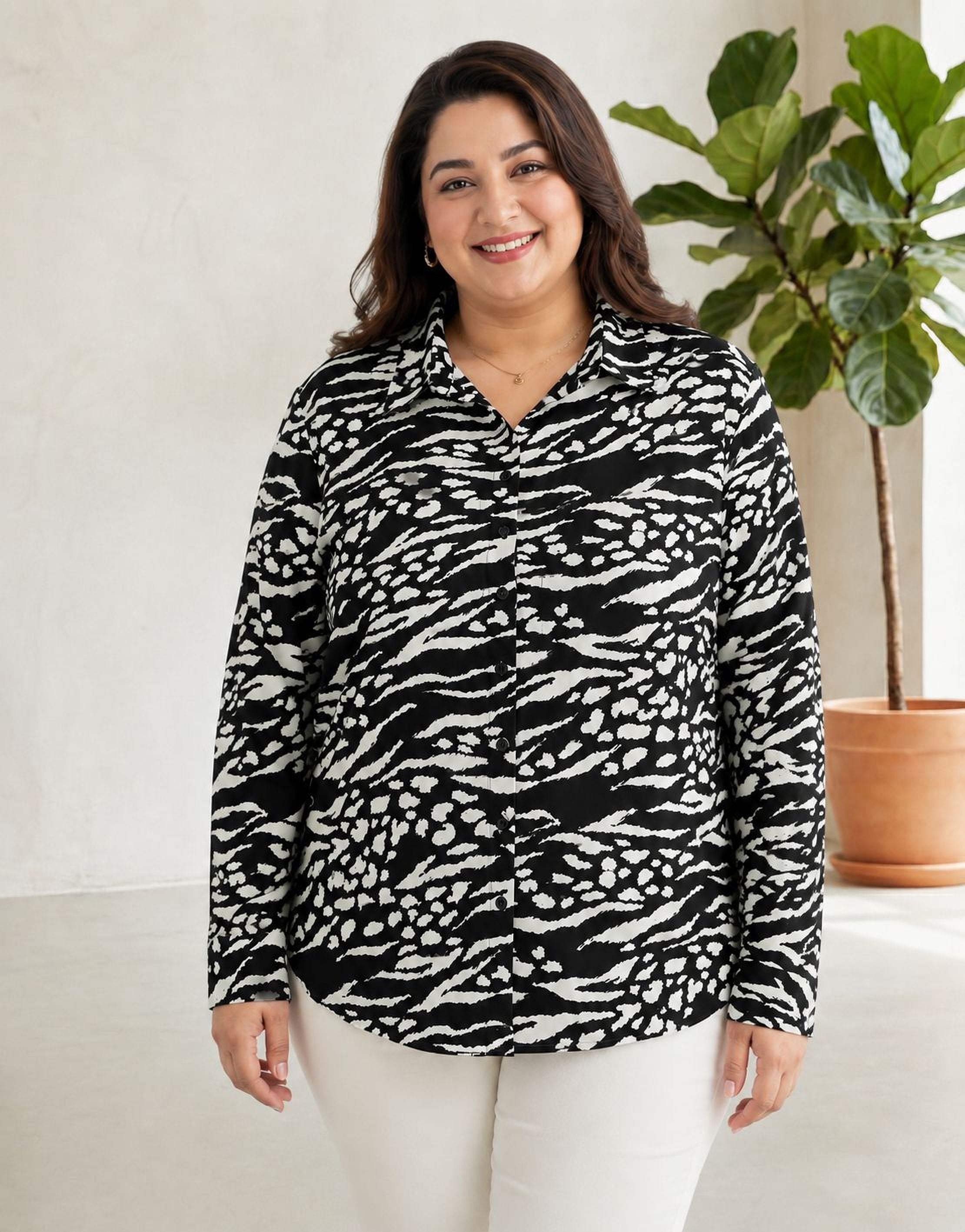 A woman wearing a black and white zebra print blouse stands in front of a potted plant, smiling at the camera.
