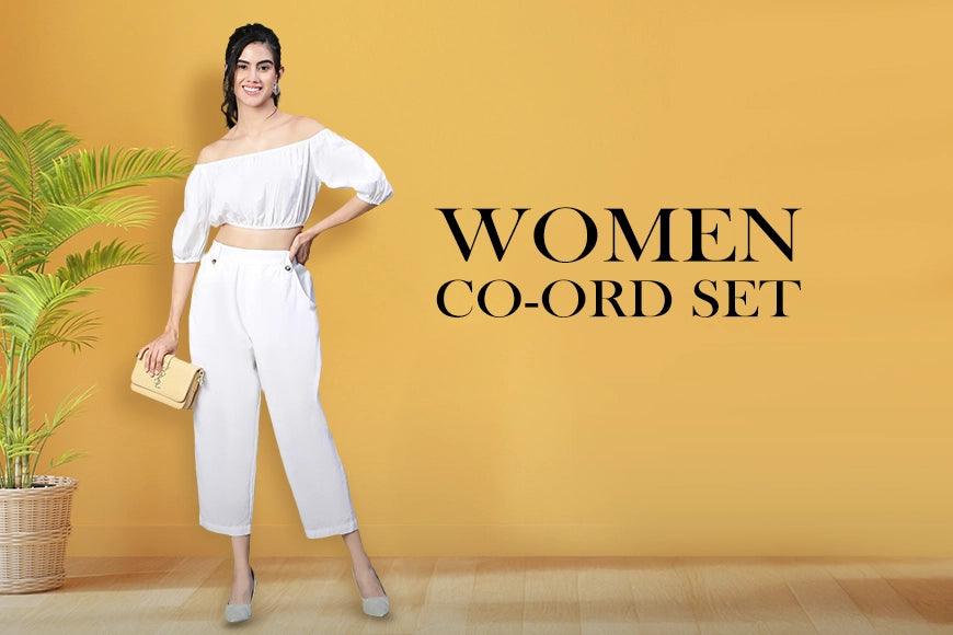 Woman in stylish white co-ord set, off-shoulder crop top and pants, holding clutch bag