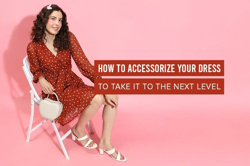 Woman in polka dot wrap dress with white heels and purse, sitting on chair, pink background