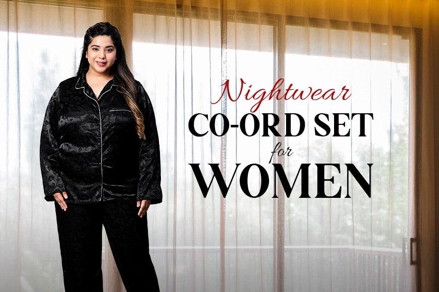 Plus size woman wearing black nightwear co-ord set, standing by window curtains