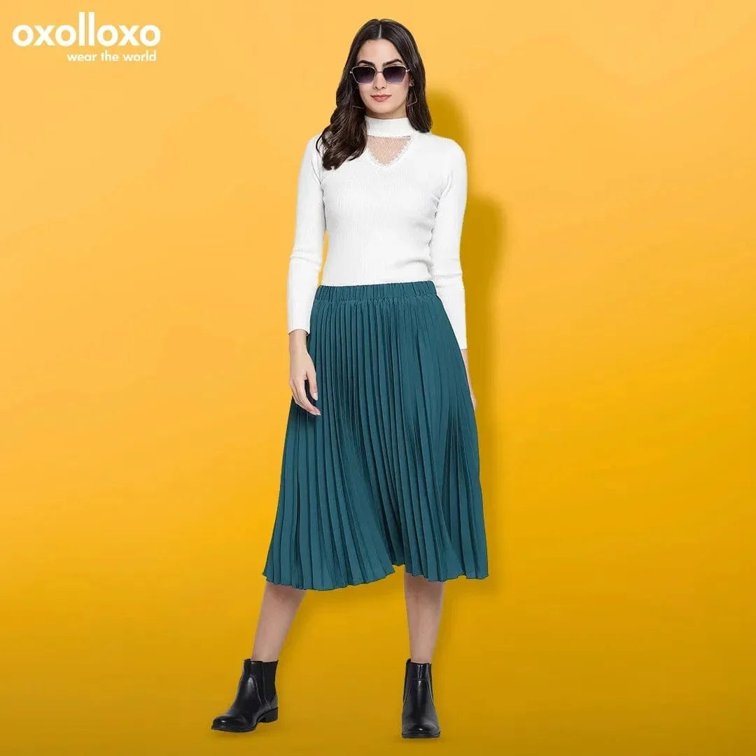 Woman in white sweater and teal pleated skirt, black ankle boots, yellow background, stylish outfit