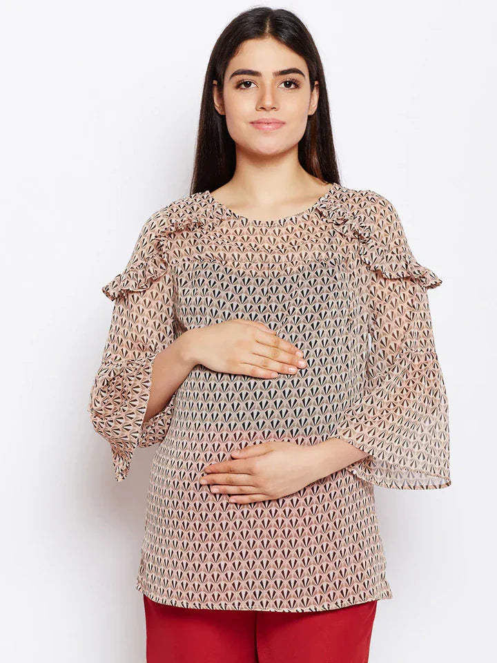 Woman wearing a patterned maternity top with flared sleeves and red pants on a white background