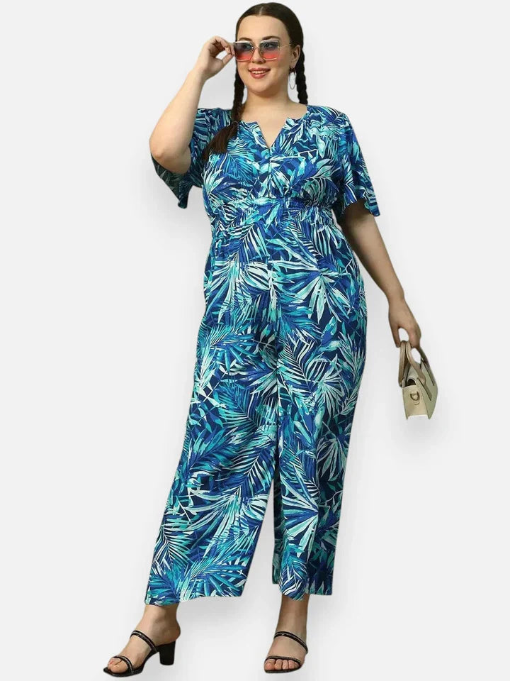 Woman wearing plus size blue tropical print jumpsuit, holding a handbag, with sandals
