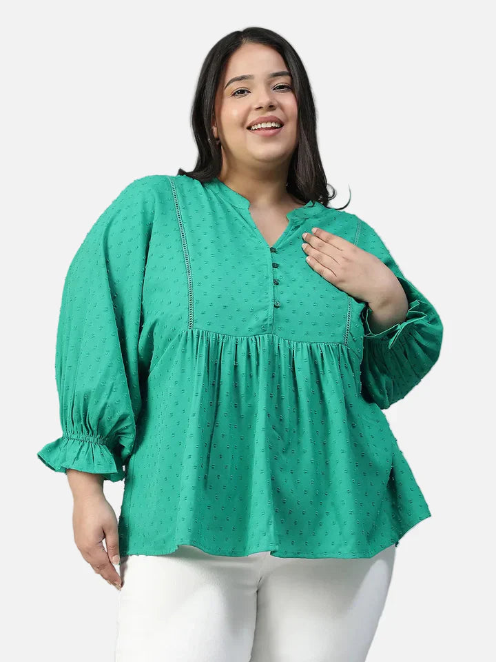Plus size woman in a teal textured long sleeve peplum top and white pants, smiling