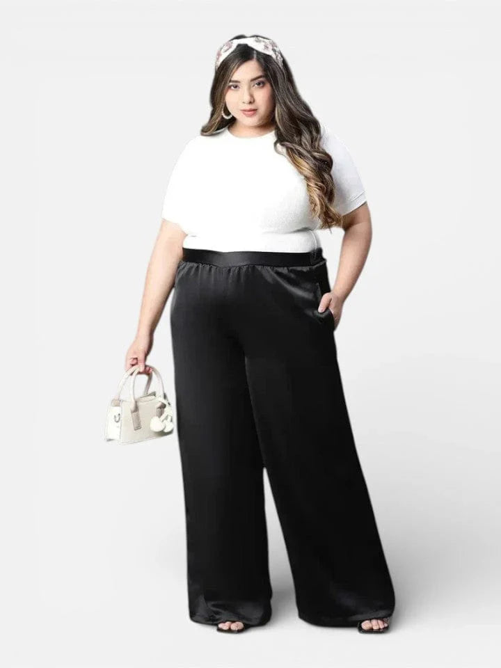 Plus size woman in white top and black wide leg pants holding a handbag, fashion clothing