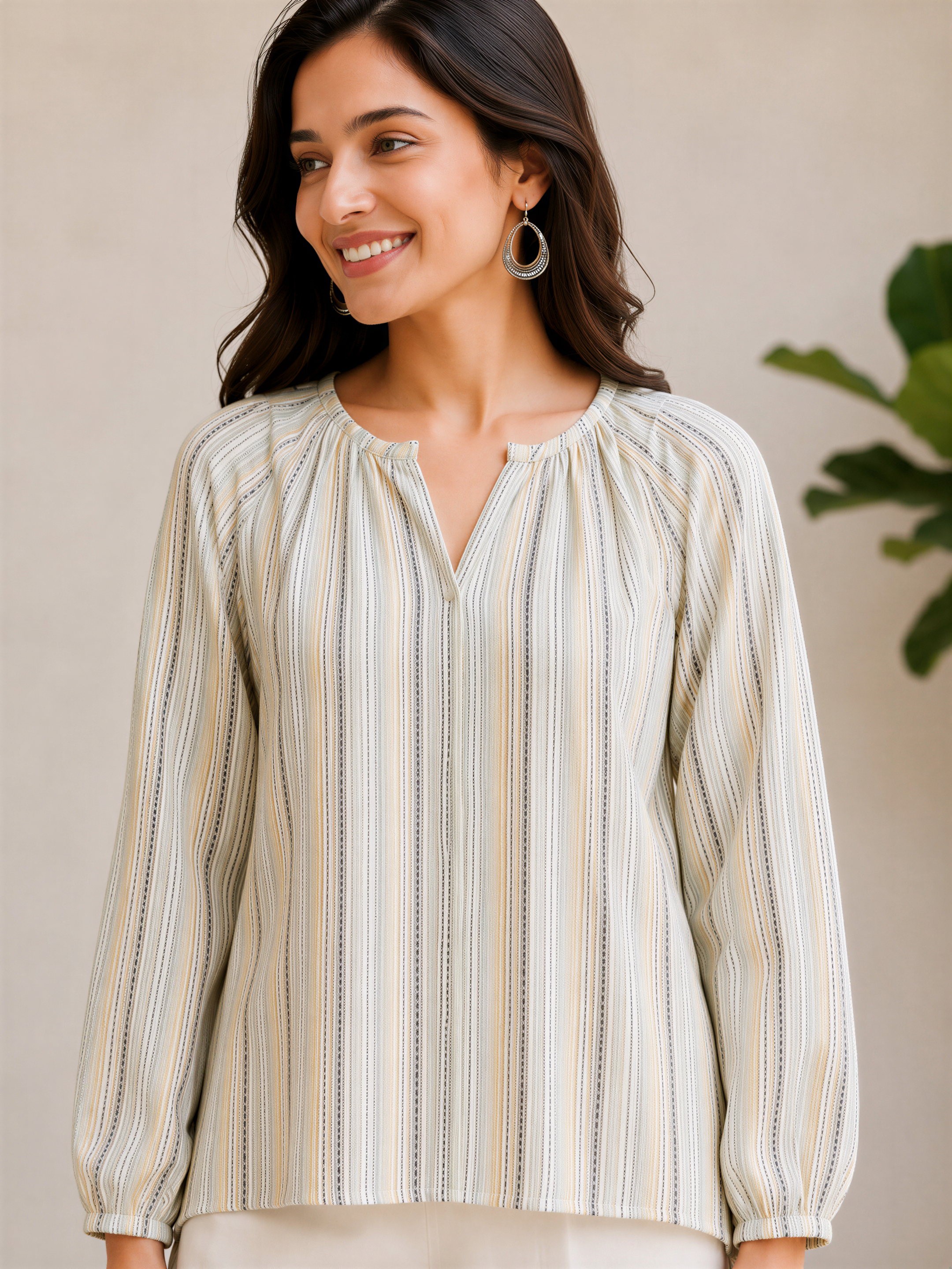 A woman with long dark hair is smiling and wearing a striped blouse with a v neck and long sleeves.