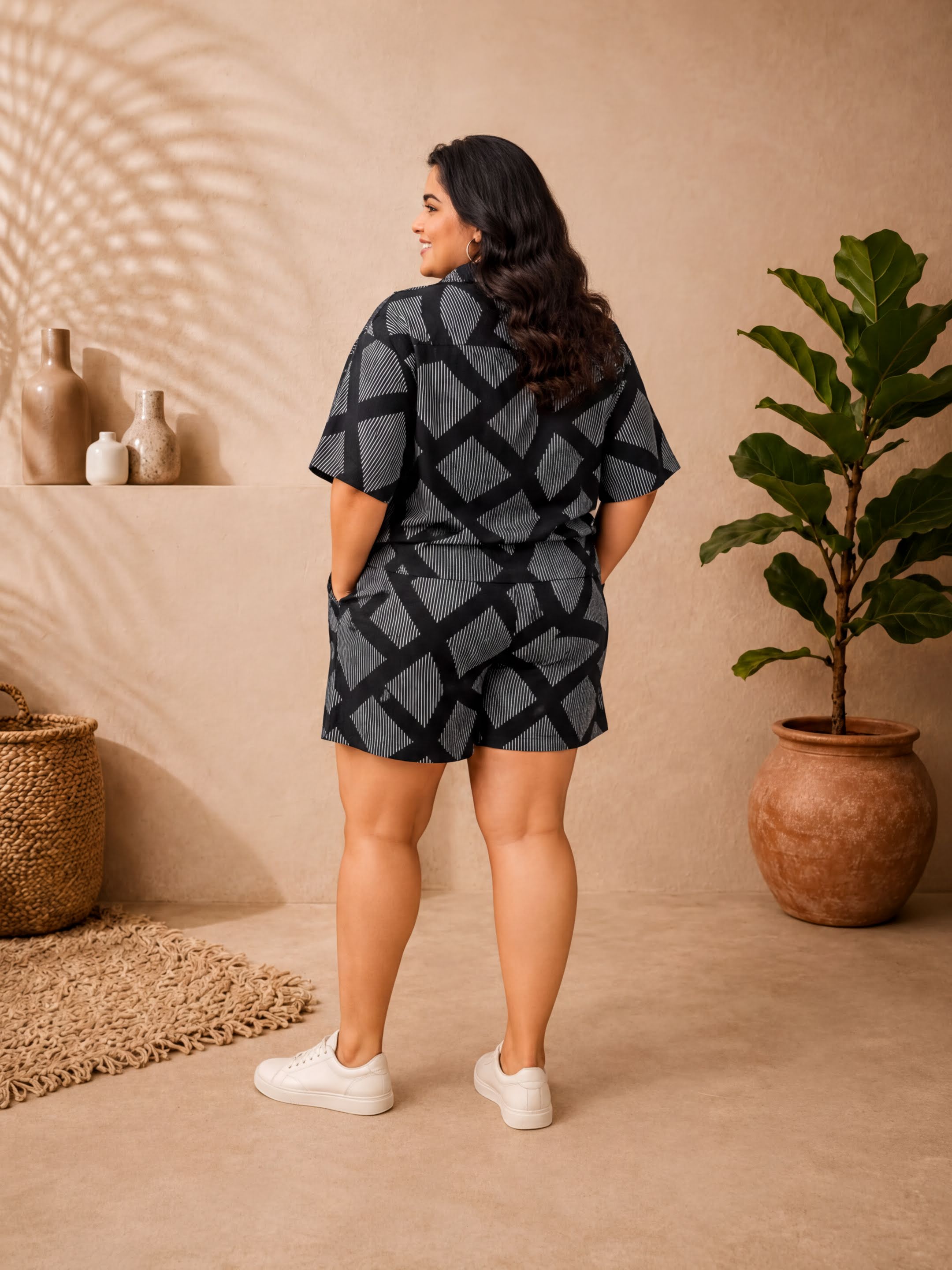A woman wearing a black and gray patterned outfit stands in a room with a beige wall, a woven basket, and a potted plant.