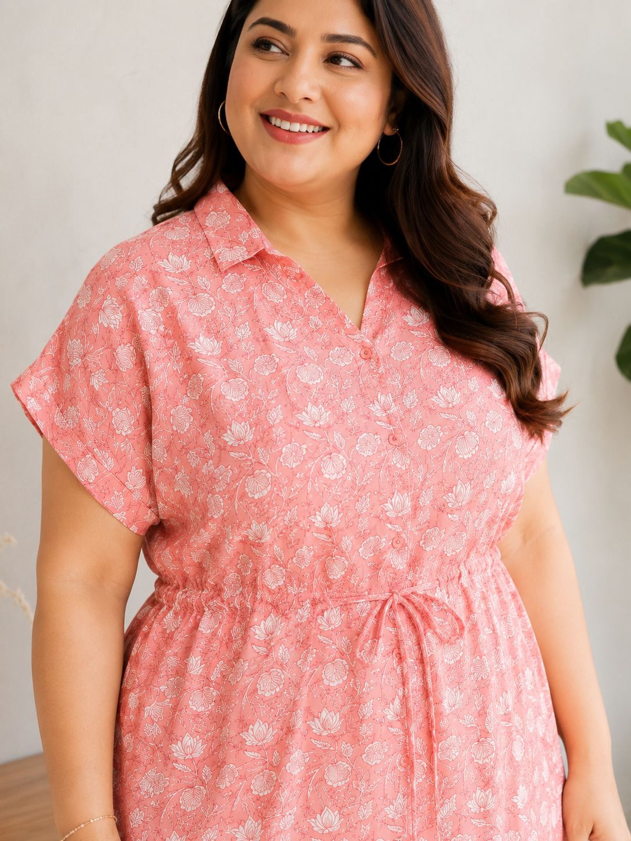 A woman with long brown hair is smiling and wearing a pink floral dress.
