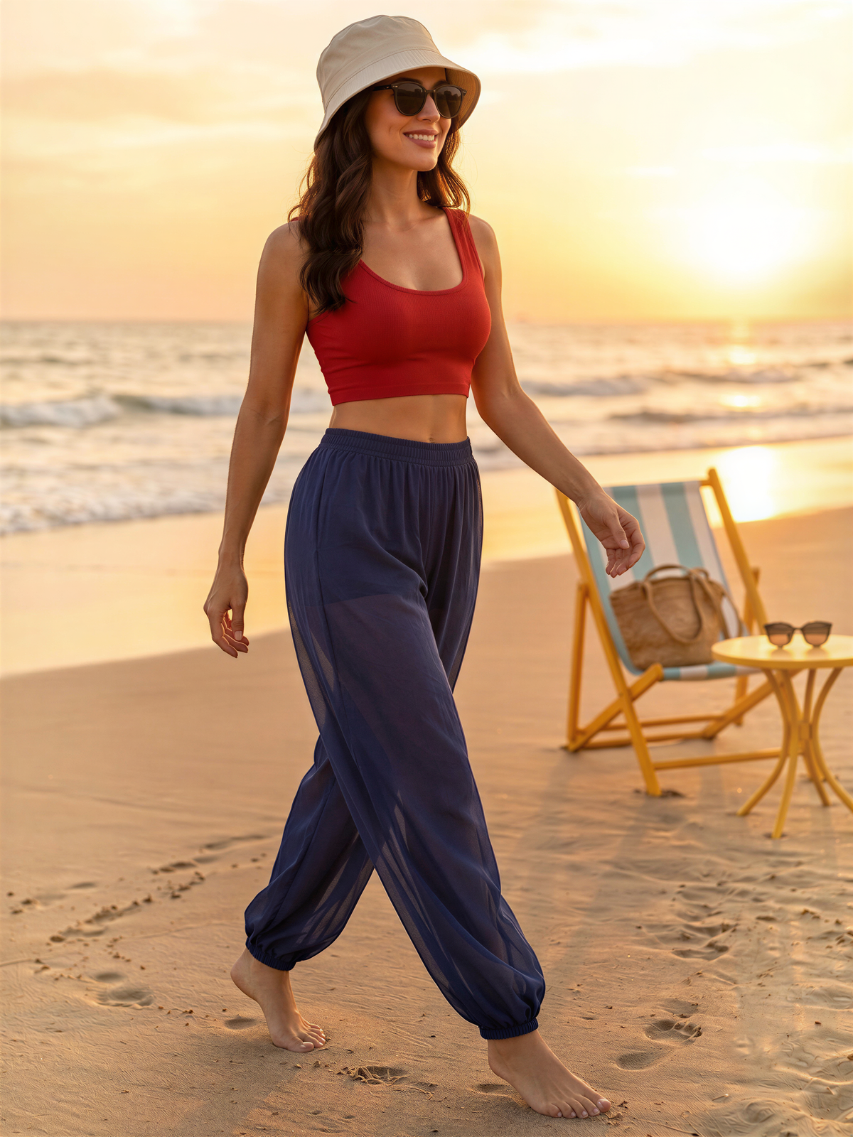 A woman in a red crop top and blue pants walks along a beach during sunset, with a beach chair and sunglasses visible in the background.