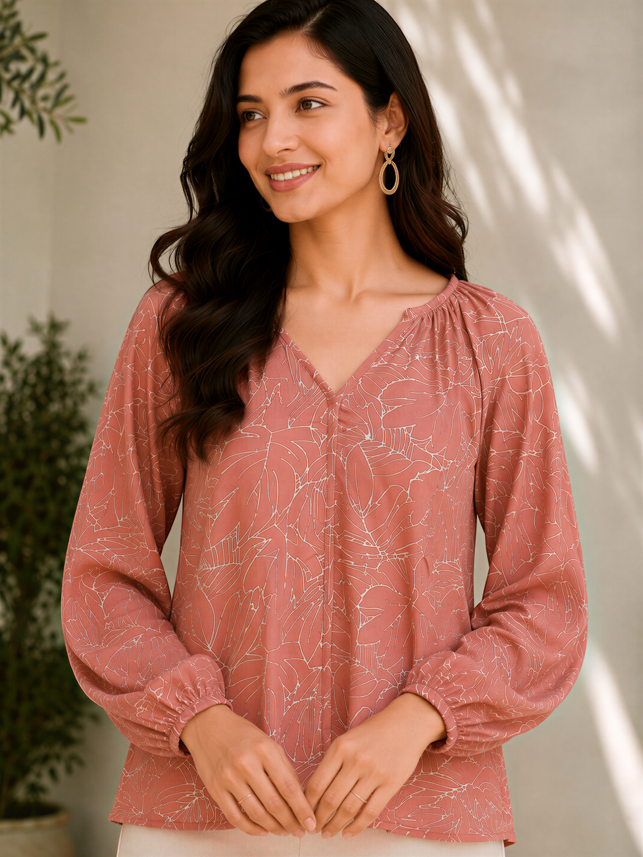 A woman with long dark hair wearing a pink blouse with leaf patterns, smiling and looking to the side.