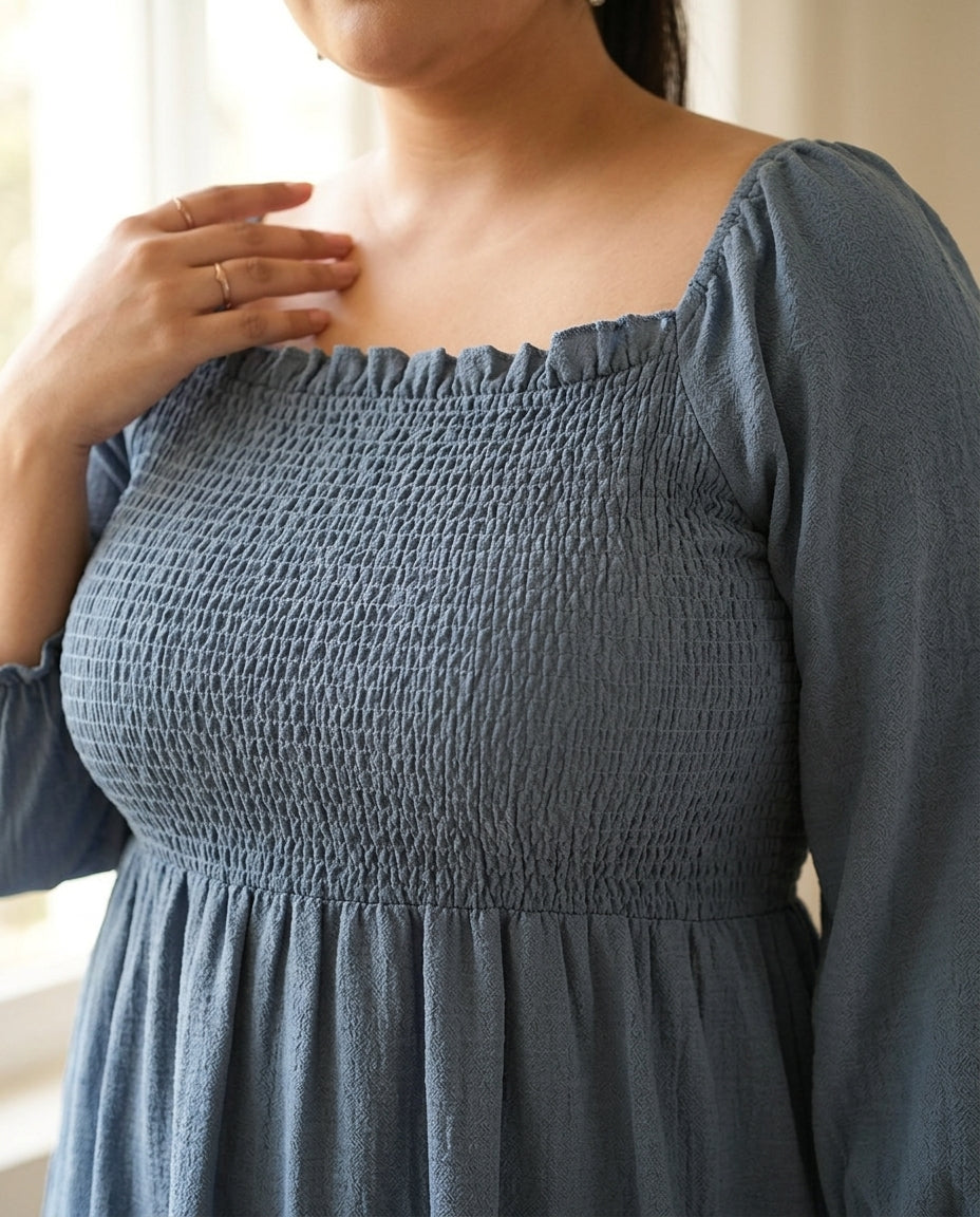 Woman wearing a plus size blue smocked long sleeve square neck dress indoors