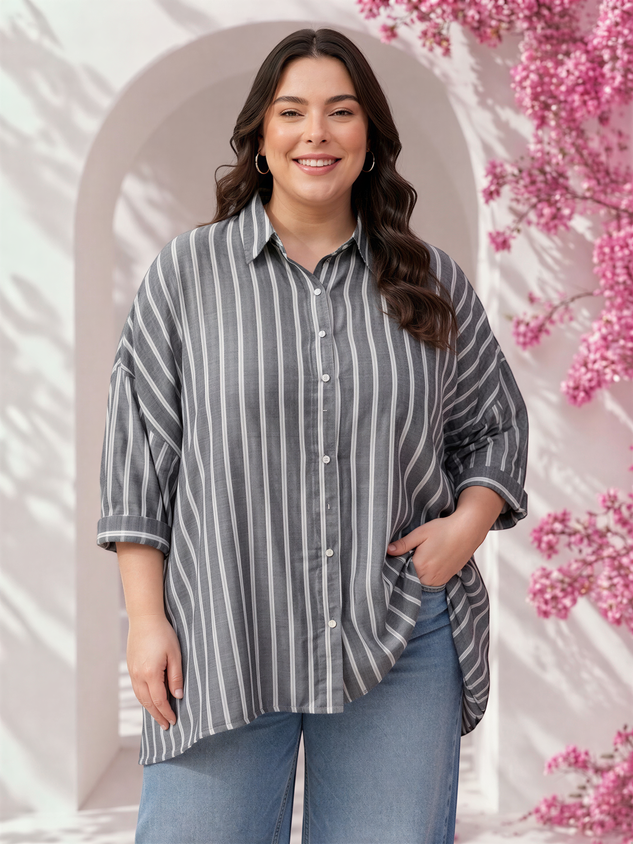 A woman with long brown hair is smiling and posing in front of a pink floral backdrop.