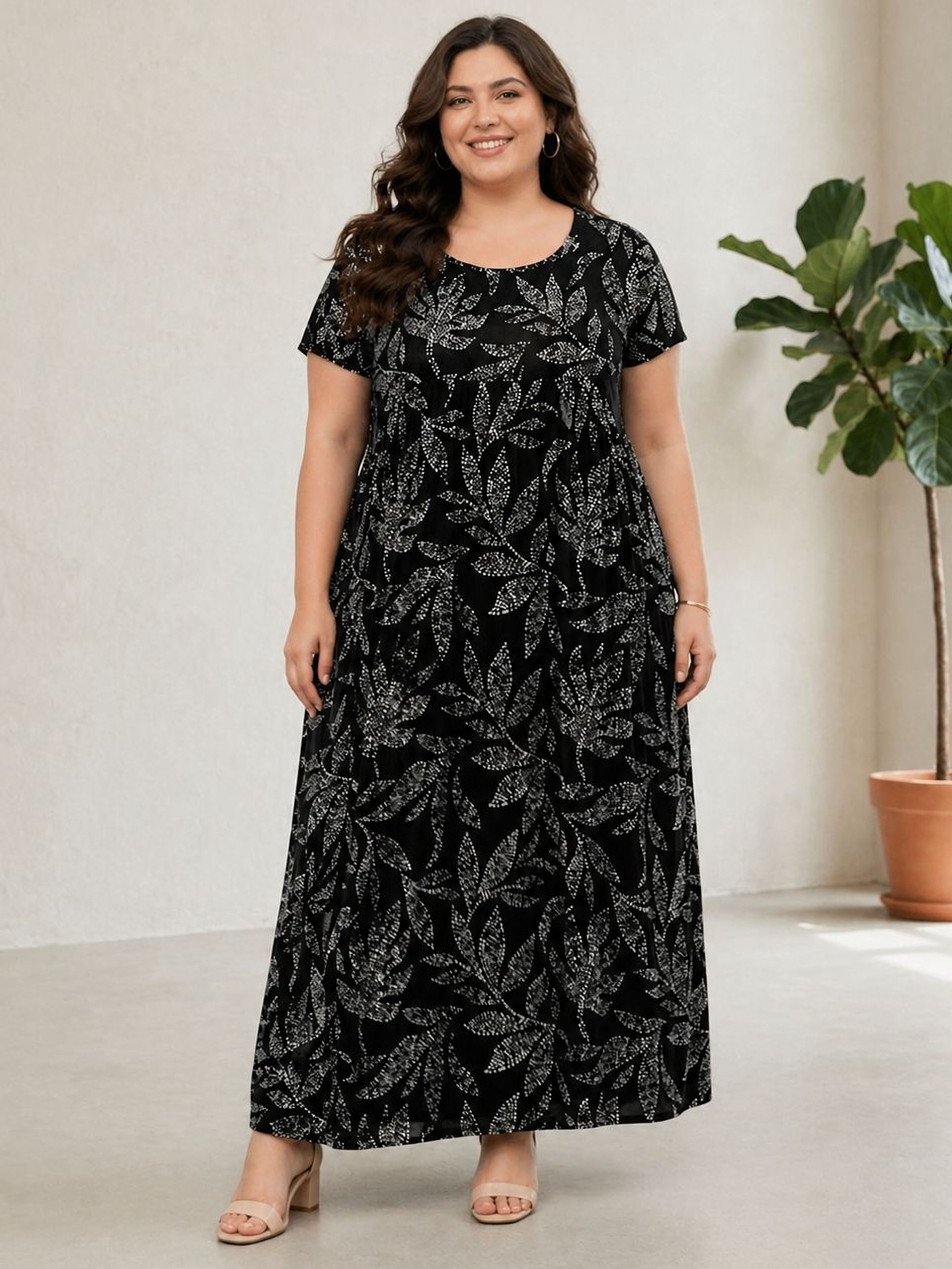 Woman wearing a black floral dress standing in a room with a plant.
