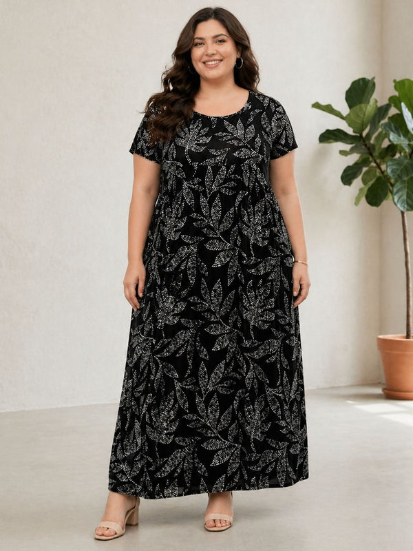 Woman wearing a black floral dress standing in a room with a plant.