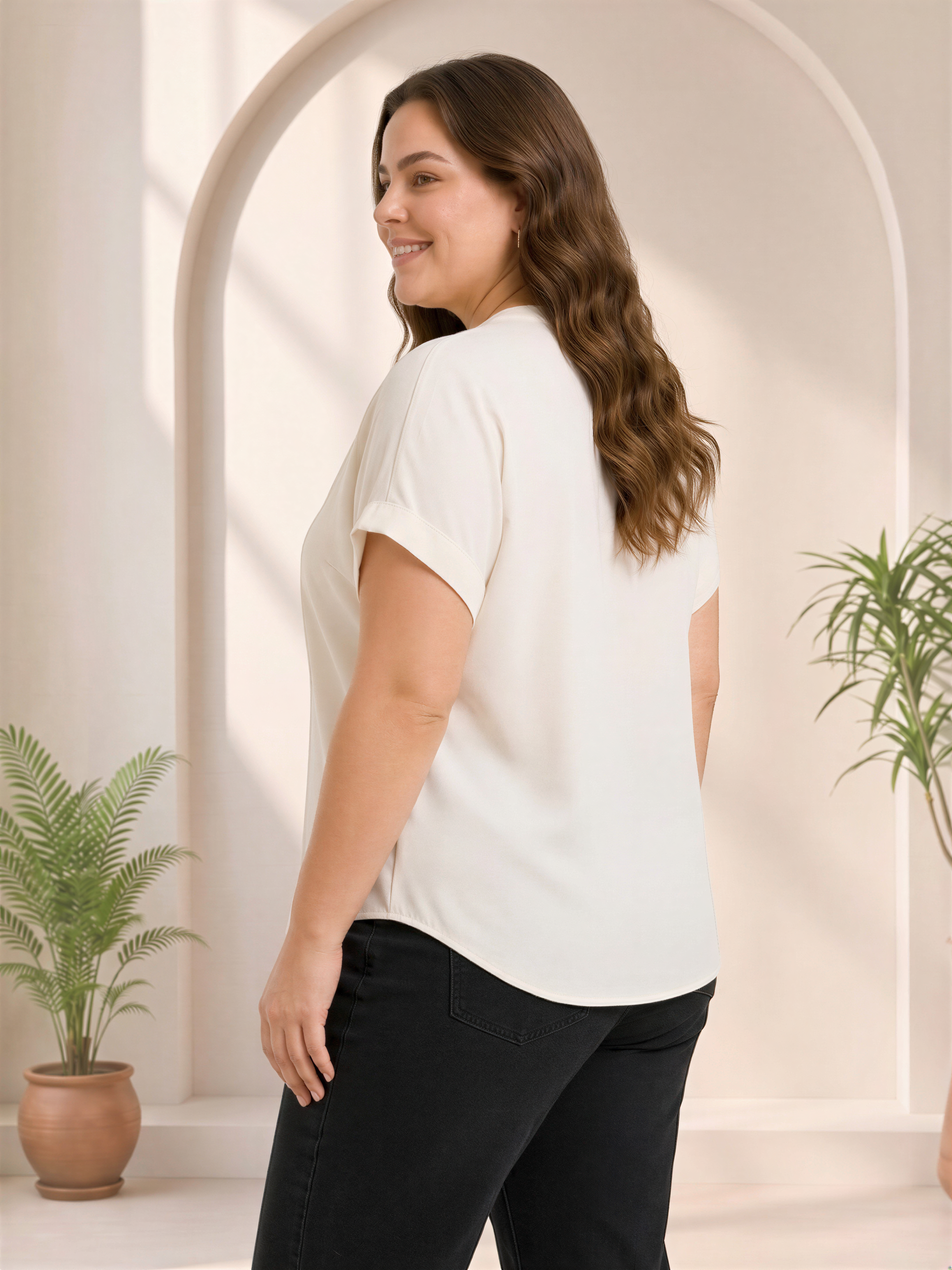 A woman with long brown hair is standing in a room with a white archway, smiling and looking to her left.