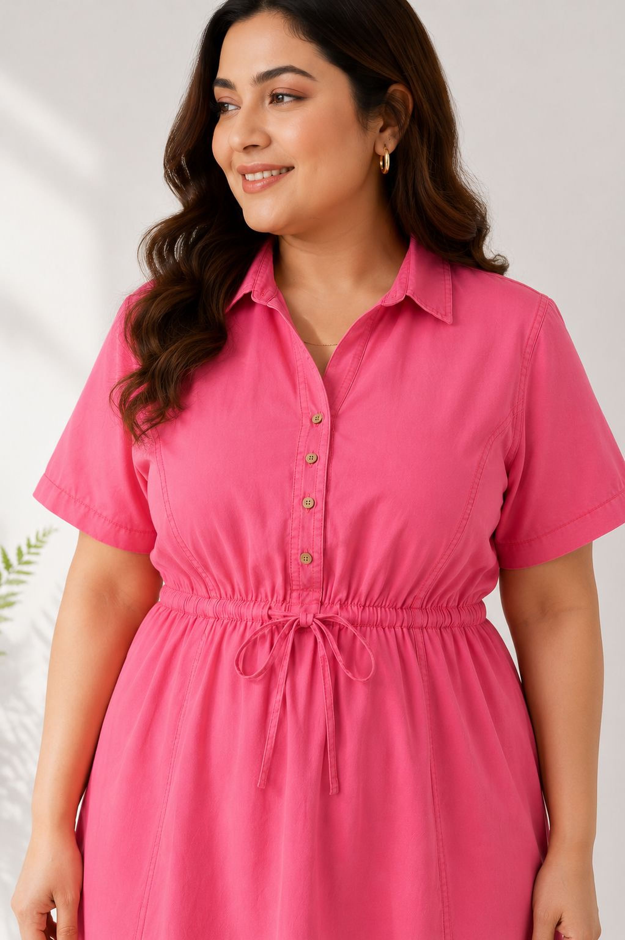 A woman with long brown hair is wearing a bright pink dress and smiling at the camera.