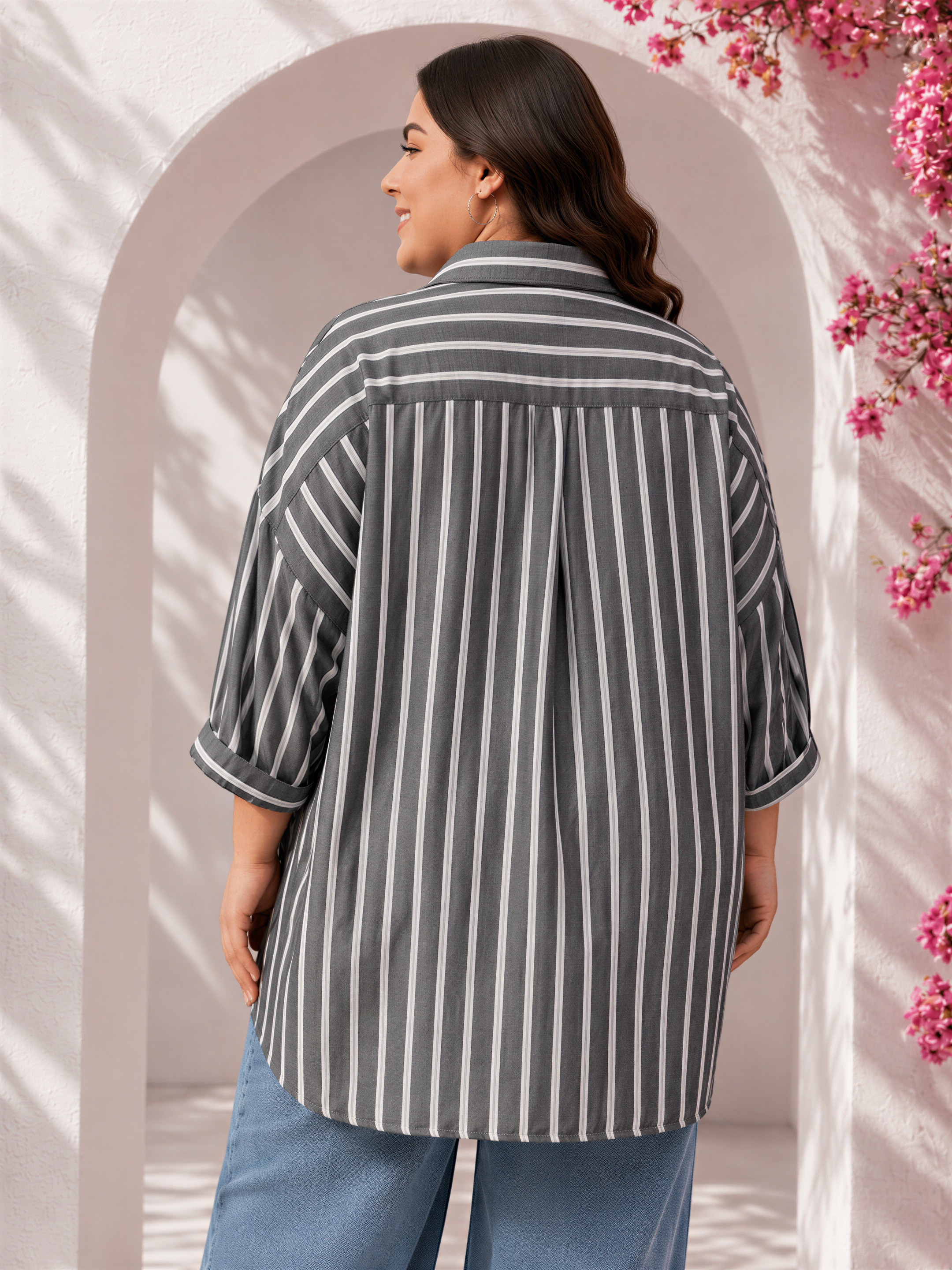 A woman wearing a gray and white striped shirt stands in front of a pink floral archway.