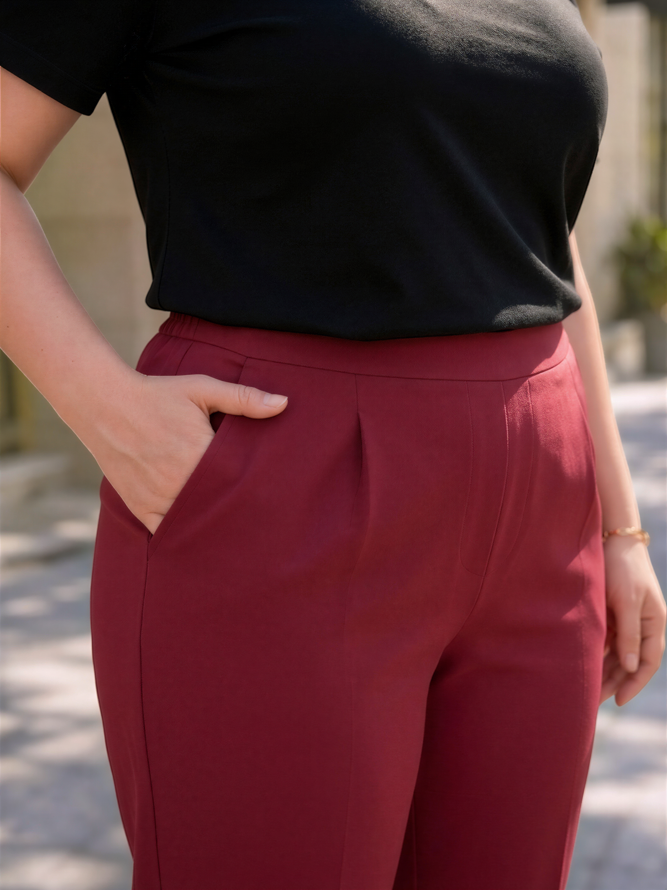 A person wearing a black top and red pants stands outdoors.