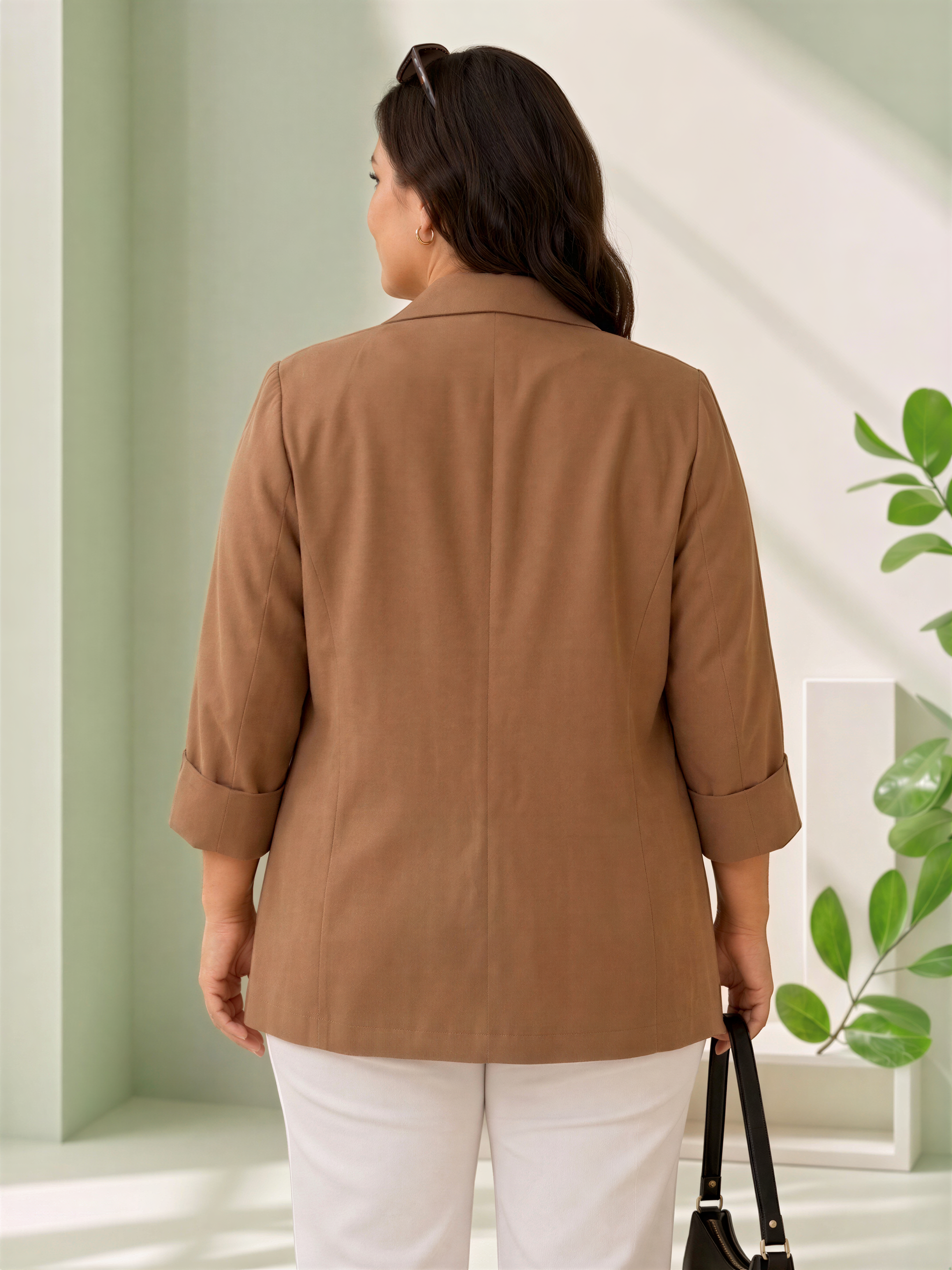 a woman wearing a brown blazer standing in a room with a green wall and a plant.