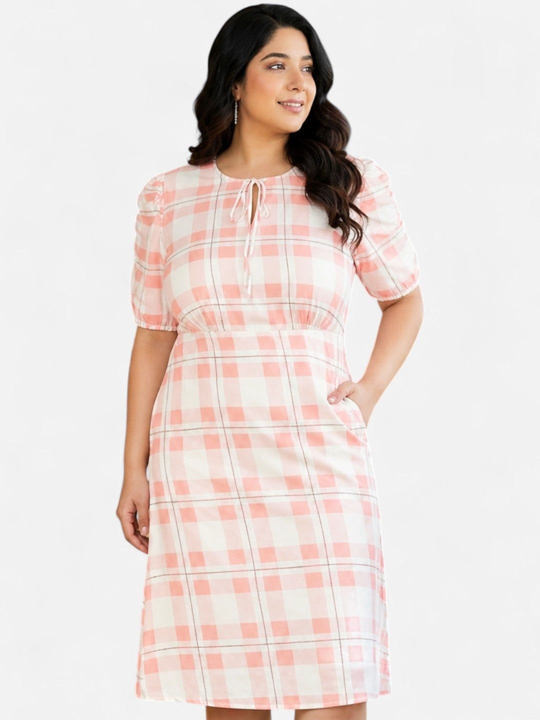 A woman wearing a pink and white plaid dress with a tie detail, smiling and looking to the side.