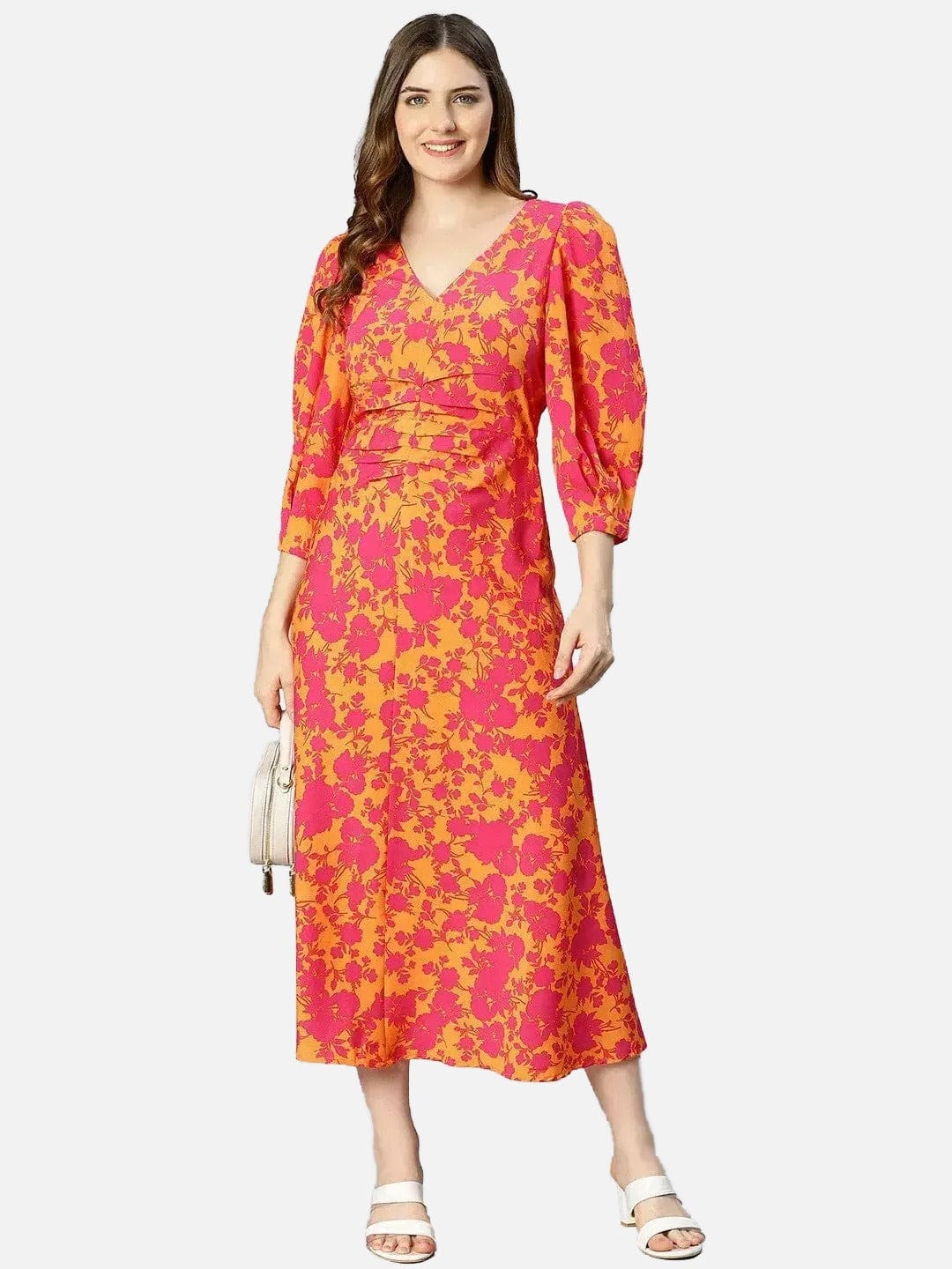 A woman wearing a long, colorful dress with a floral pattern in shades of orange and pink. She is smiling and posing for the camera.