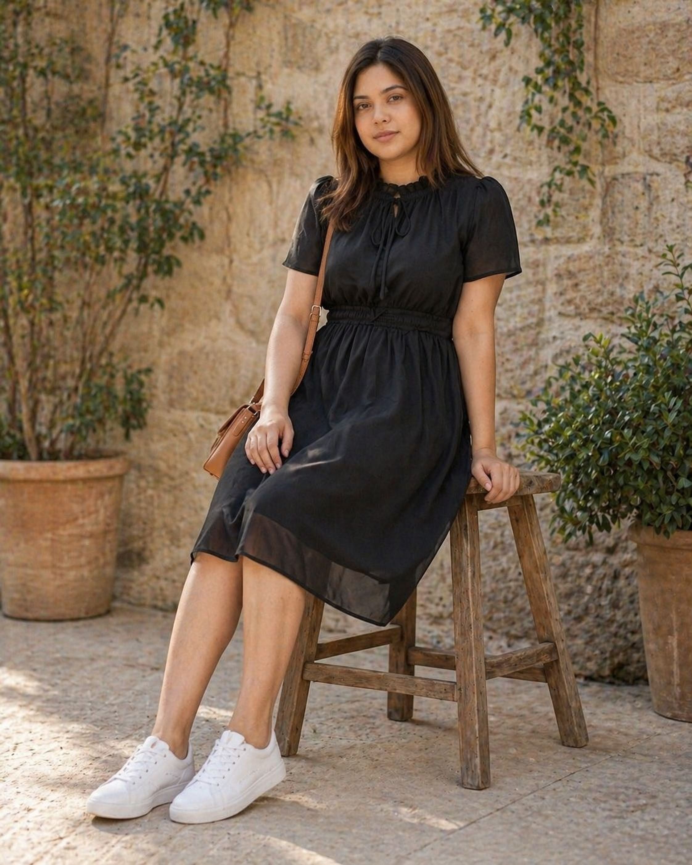 A woman wearing a black dress and high heels is smiling and looking down at her hand.
