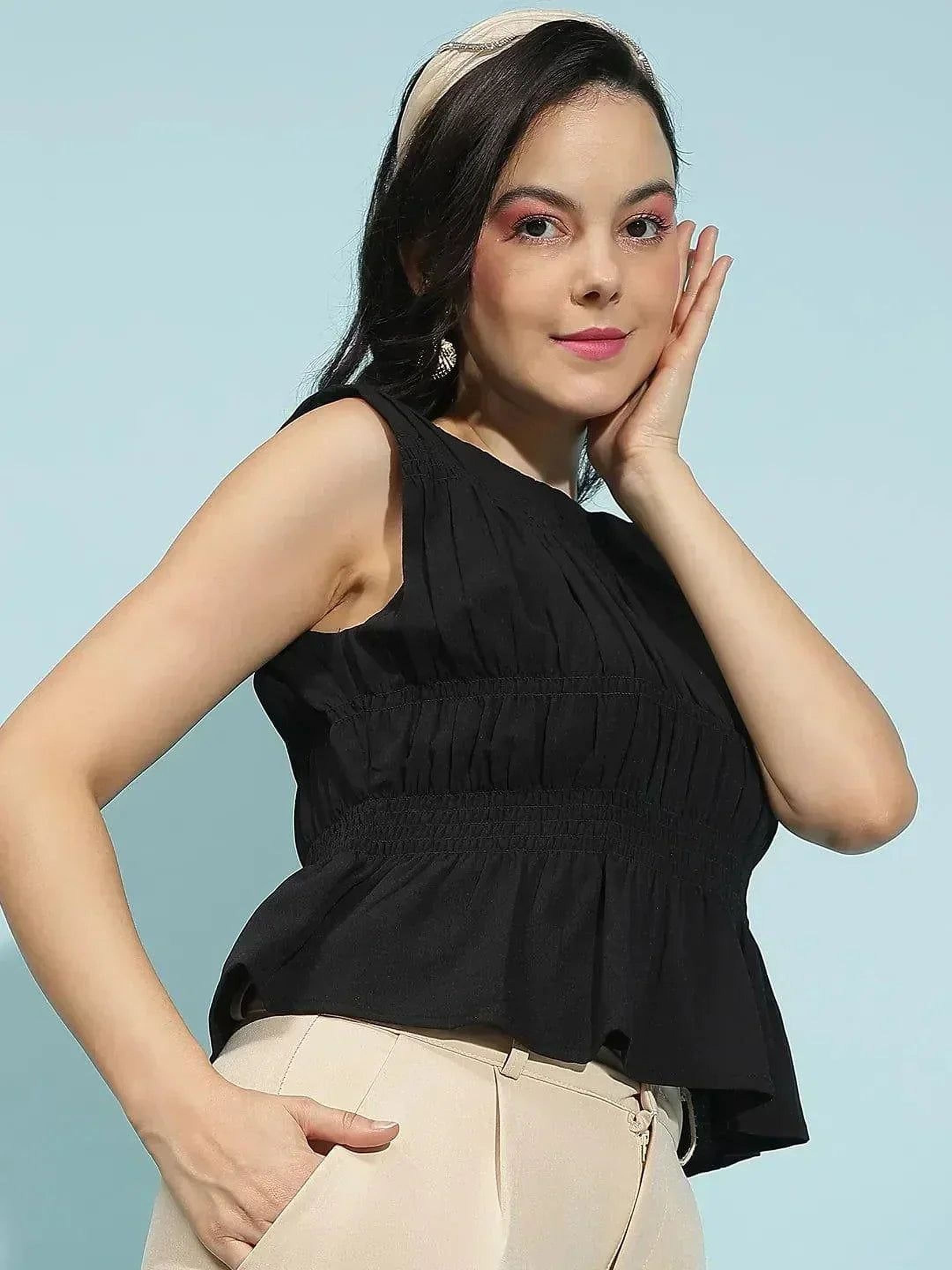 A woman with dark hair wearing a black sleeveless top and a headband is smiling and looking to the side.