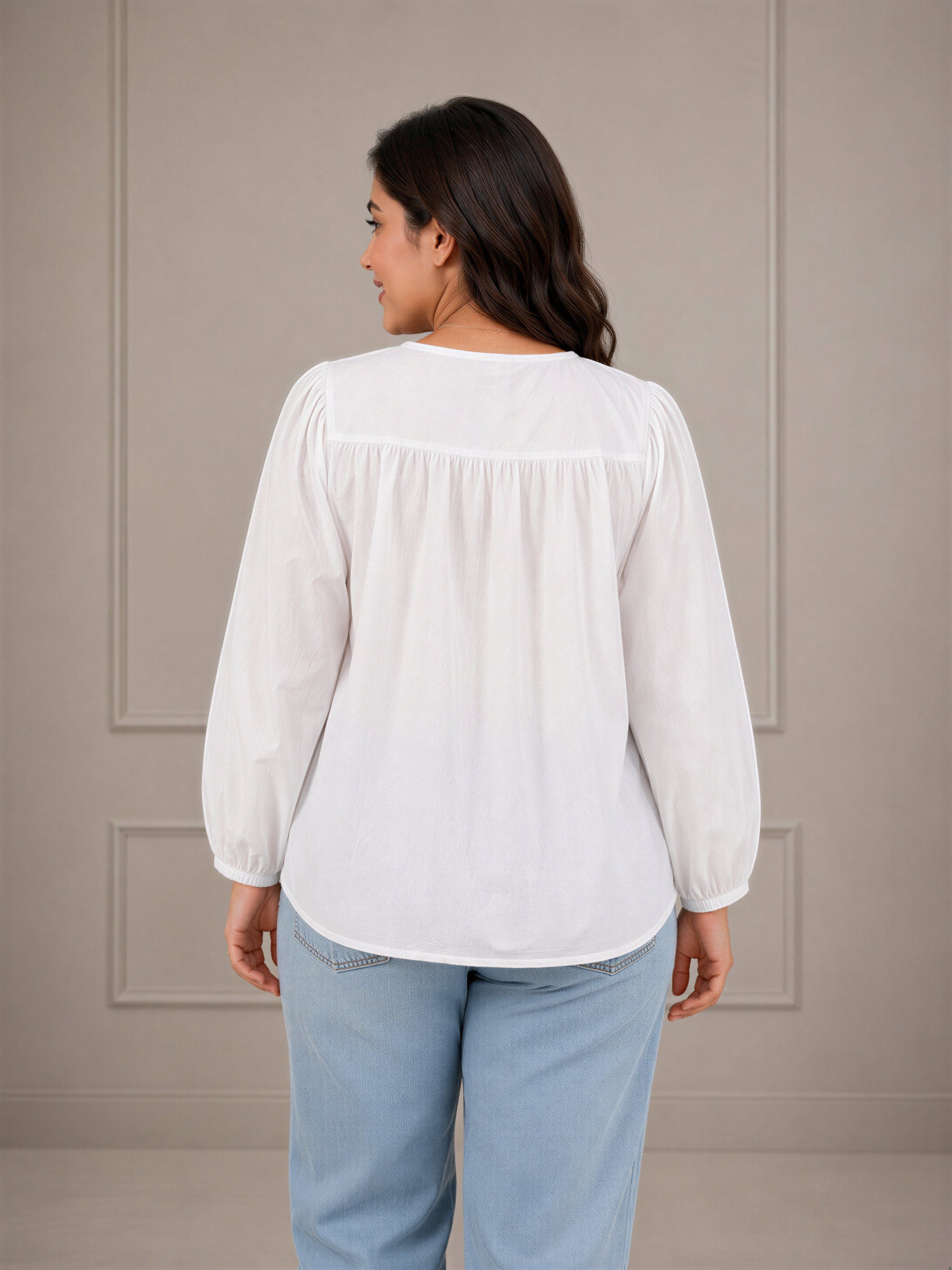 A woman wearing a white blouse and light blue jeans is facing away from the camera, with her back turned to the viewer.