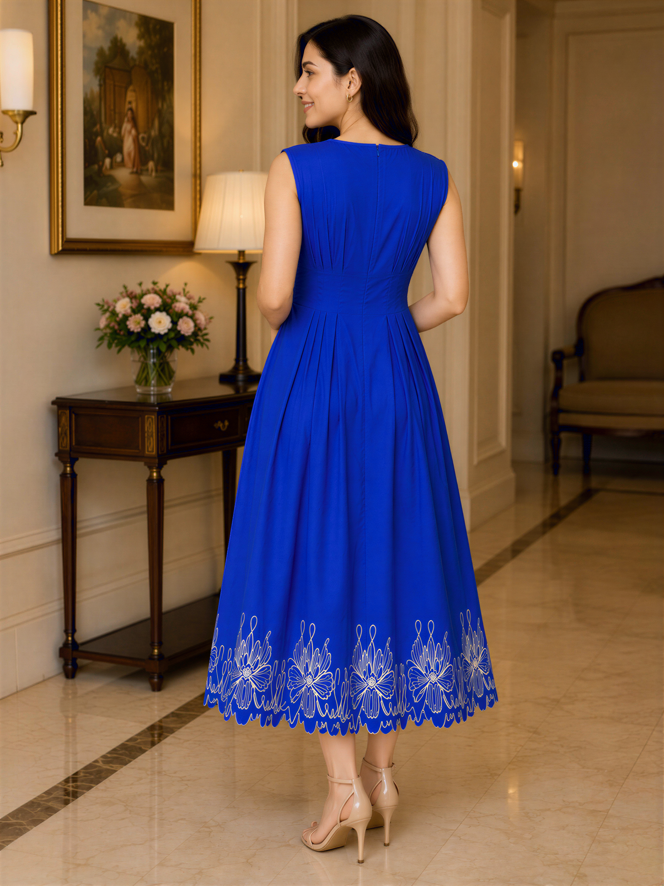 A woman wearing a blue dress with a floral pattern stands in a hallway, facing away from the camera.