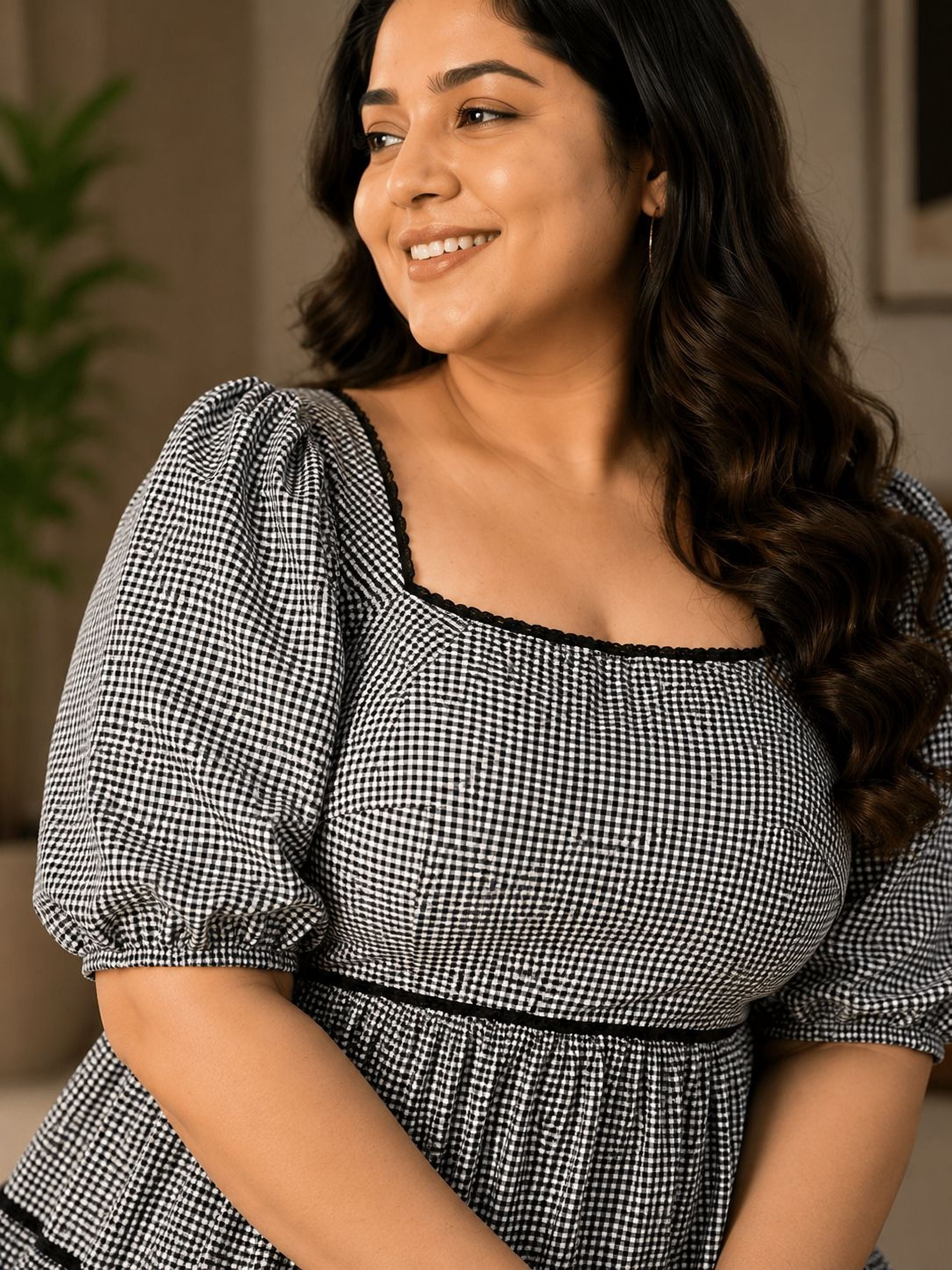 A woman with long, dark hair is smiling and looking to the side, wearing a black and white checkered dress.