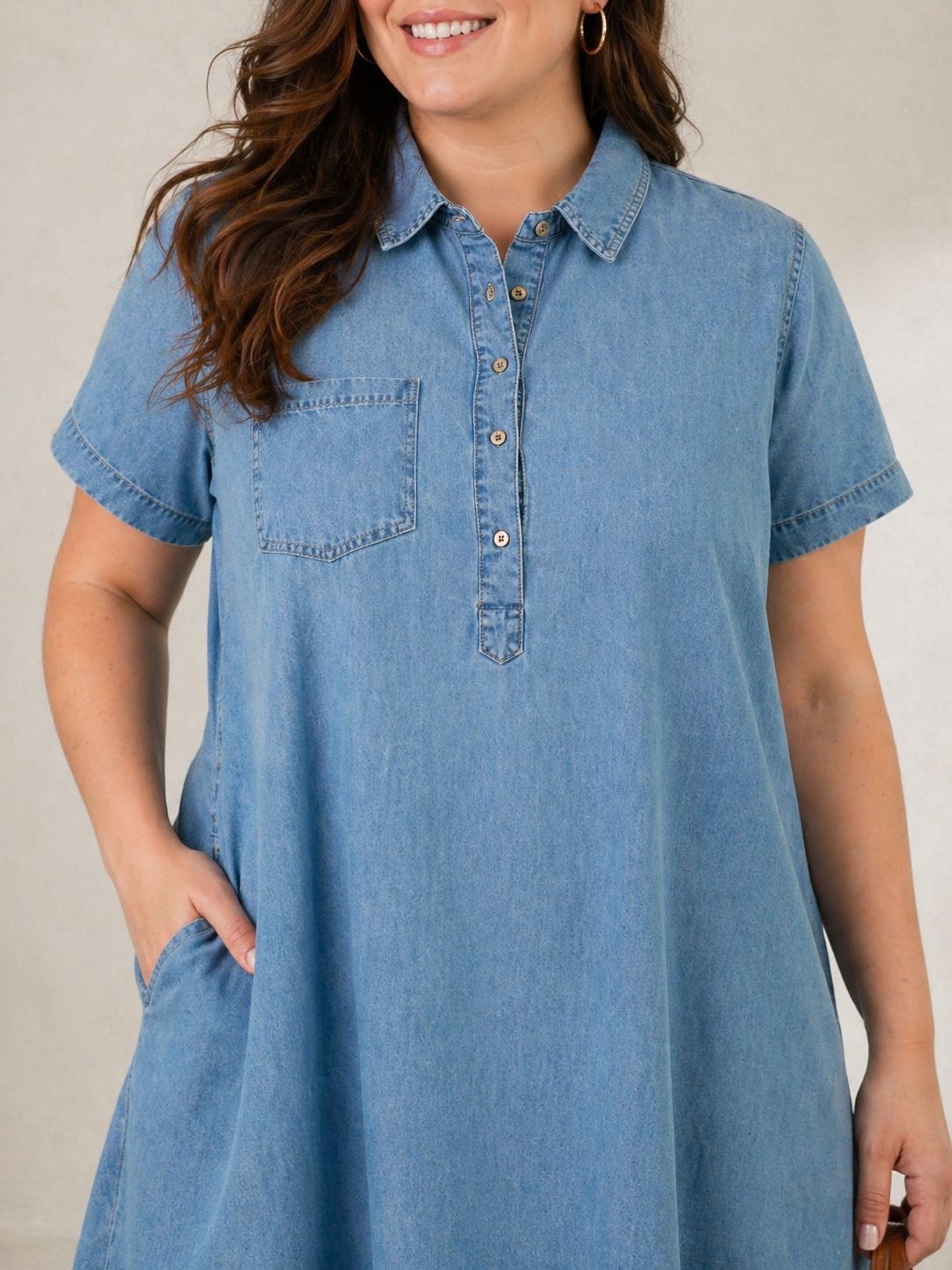 A woman wearing a blue denim dress with short sleeves and a collar, smiling at the camera.