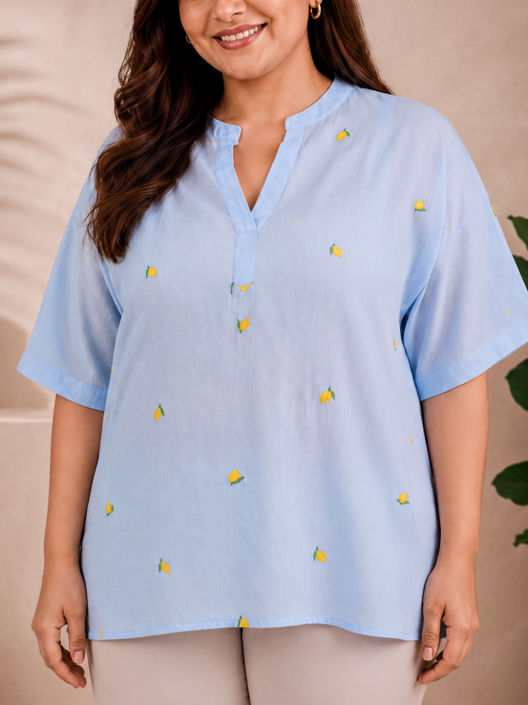 A woman wearing a light blue blouse with yellow fruit designs on it, smiling at the camera.