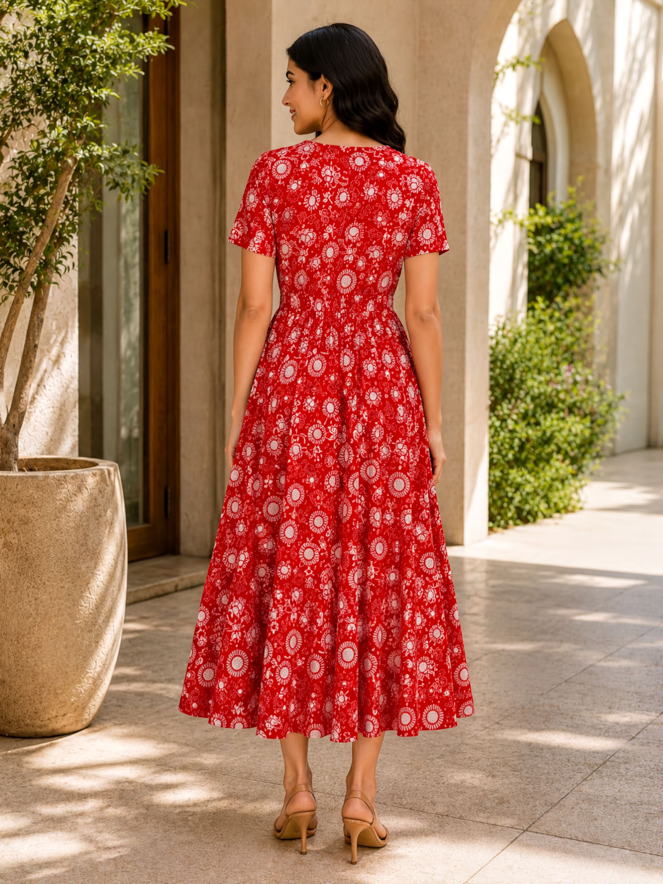 A woman wearing a red dress with a floral pattern is standing in front of a building with arched windows.