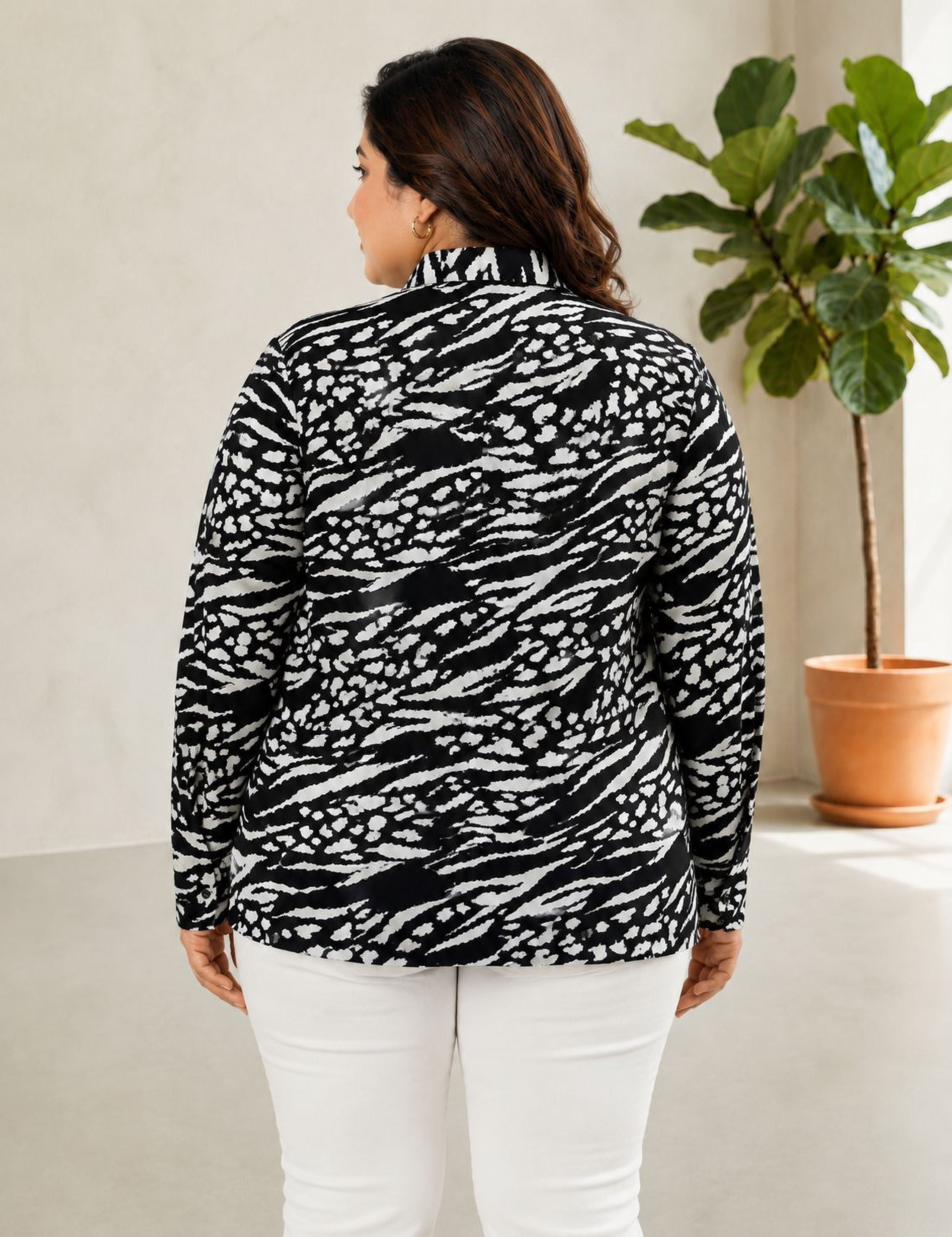 a woman wearing a black and white patterned sweater standing in a room with a potted plant in the background.