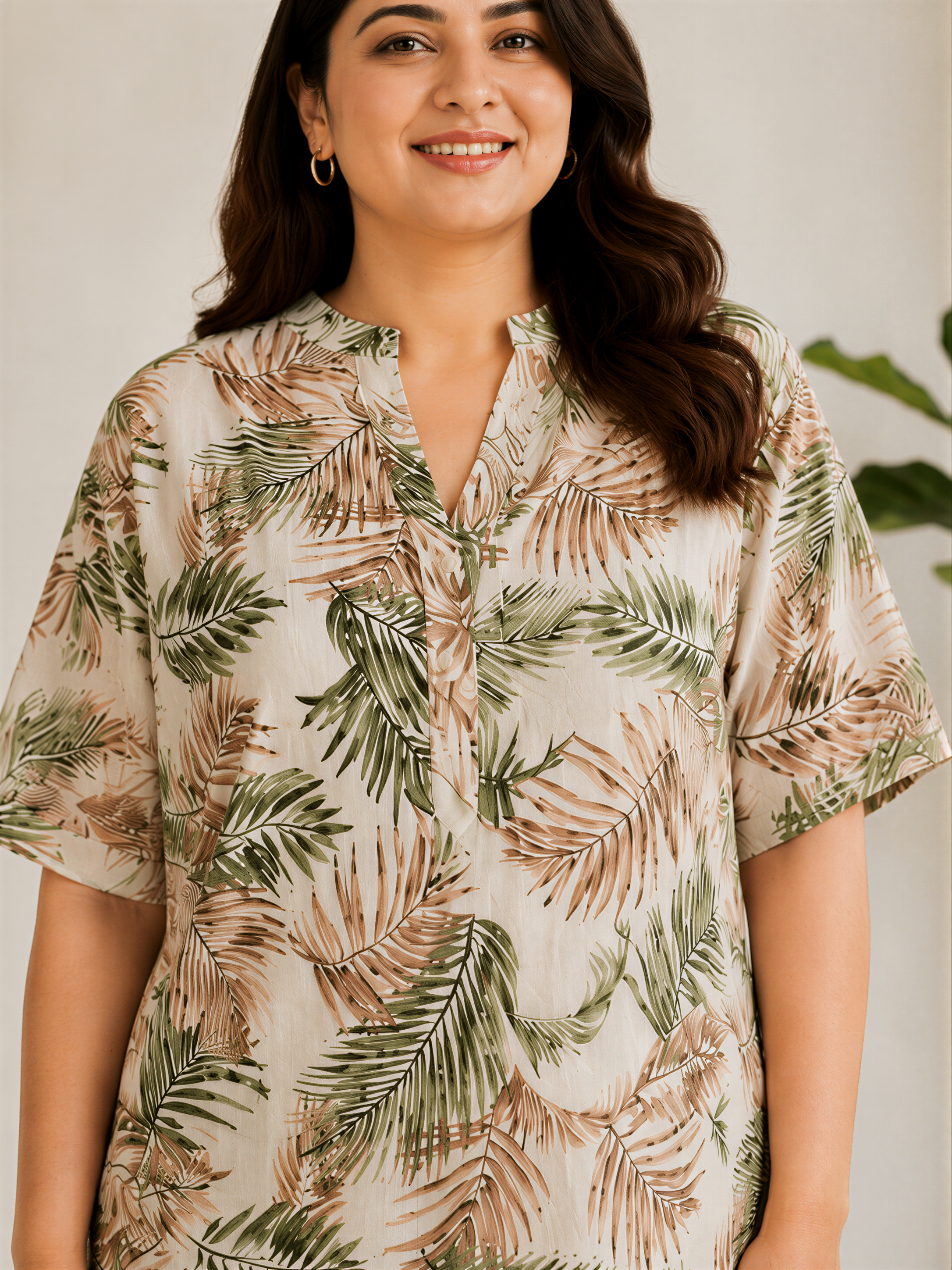 A woman wearing a white blouse with a tropical leaf print stands in front of a plain background.