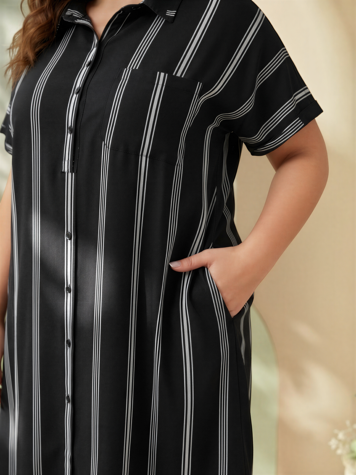 A close-up of a person wearing a black and white striped dress with short sleeves and a pocket.