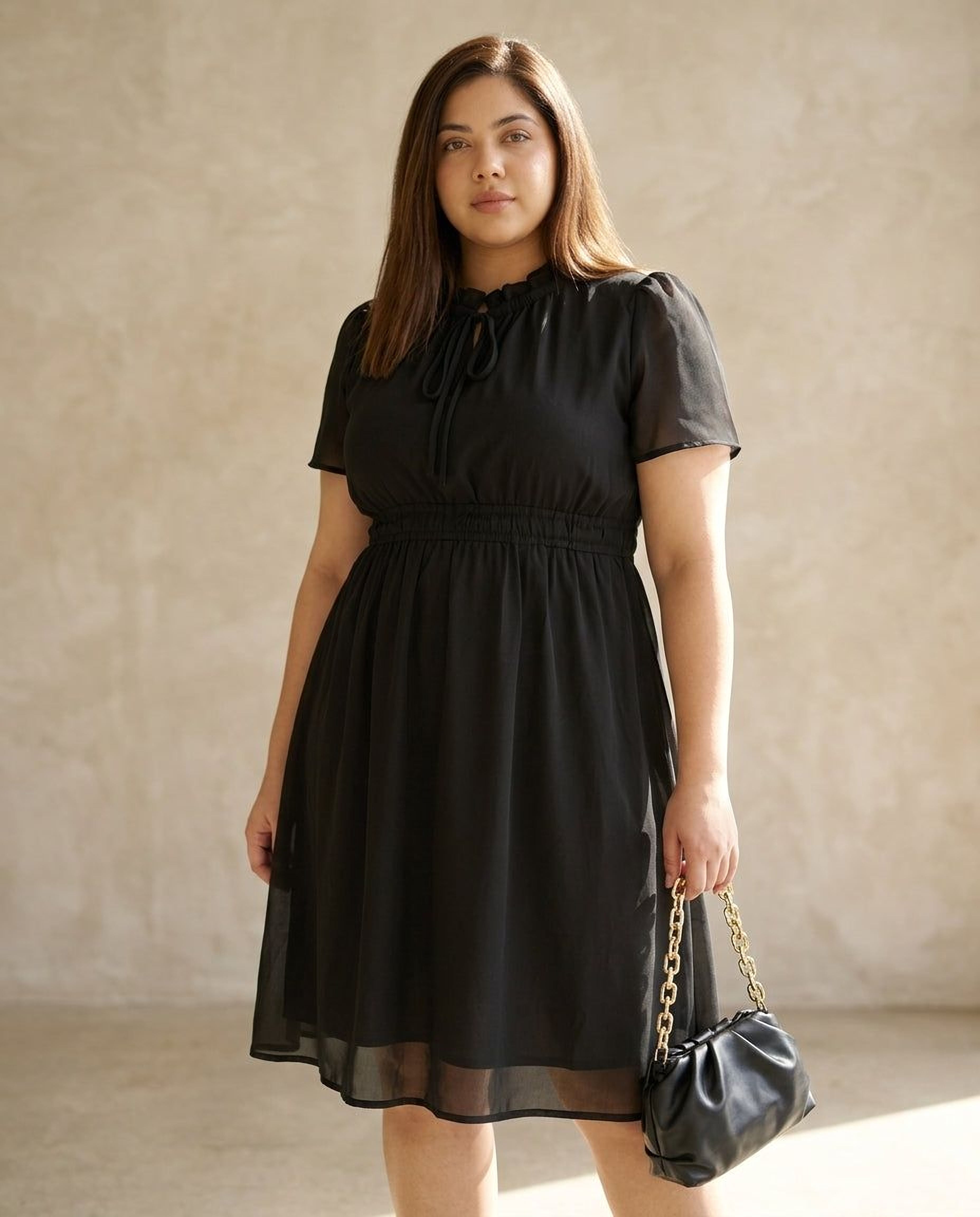 A woman wearing a black dress and high heels is smiling and looking down at her hand.