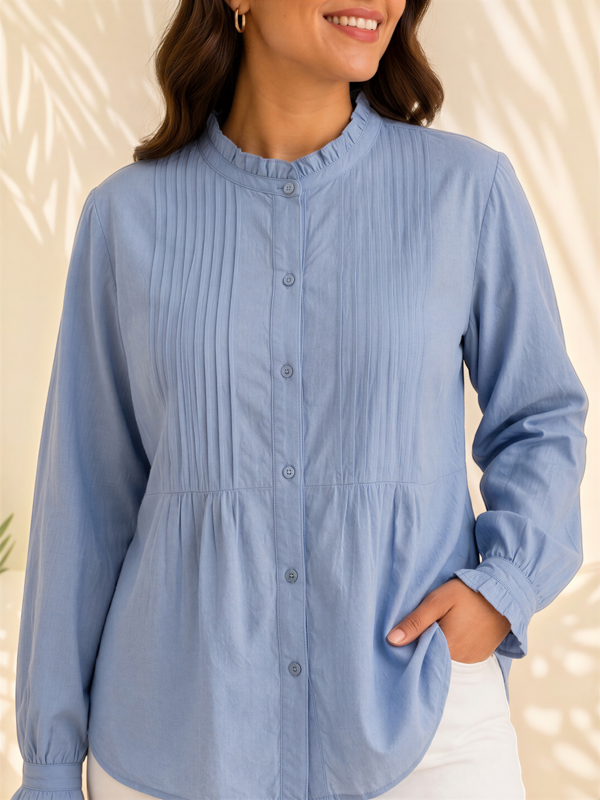A woman wearing a blue button-up shirt with a ruffled collar and long sleeves, smiling at the camera.