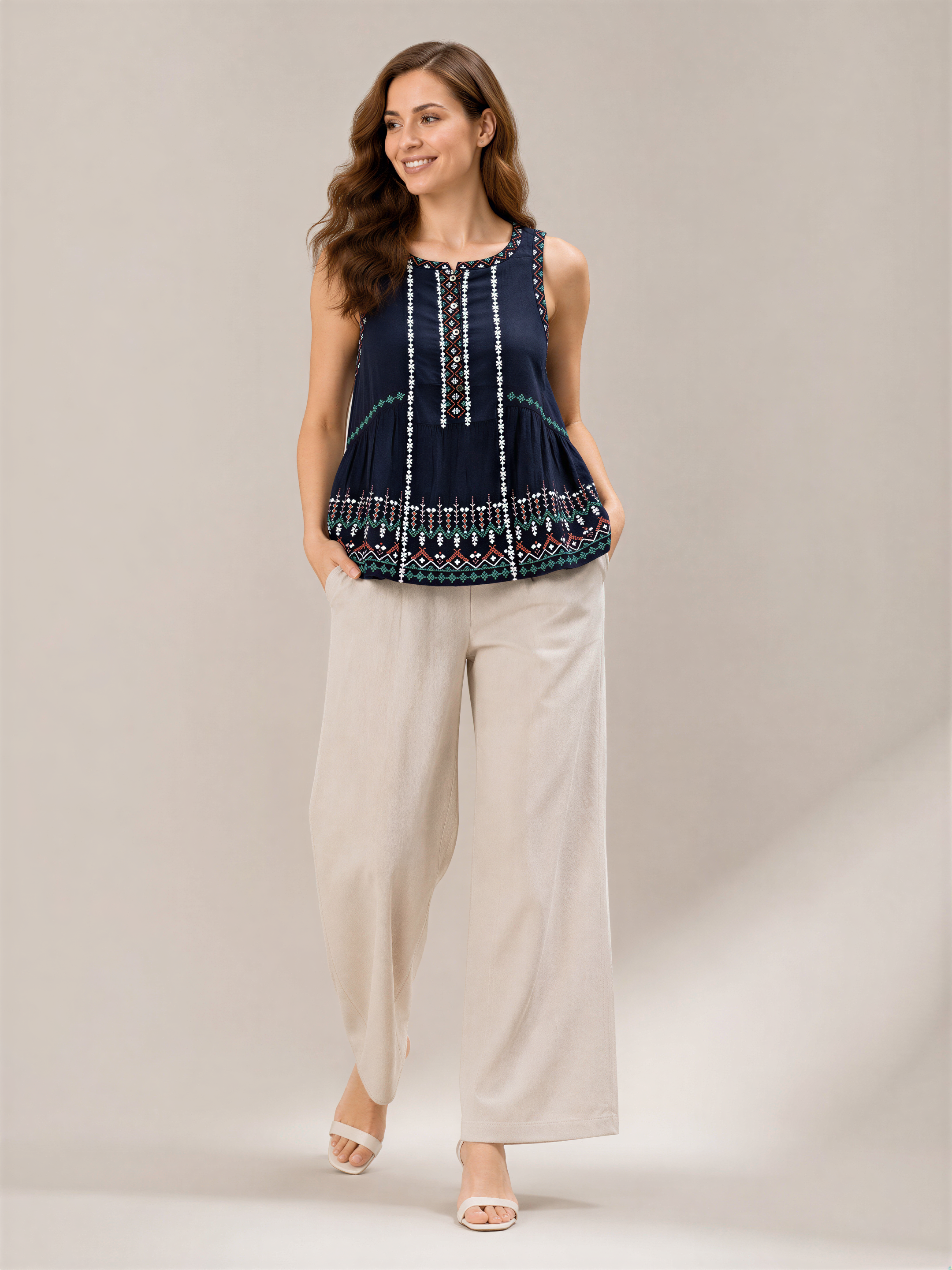 A woman wearing a navy blue top with a floral pattern and beige wide-leg pants, smiling and standing against a plain background.