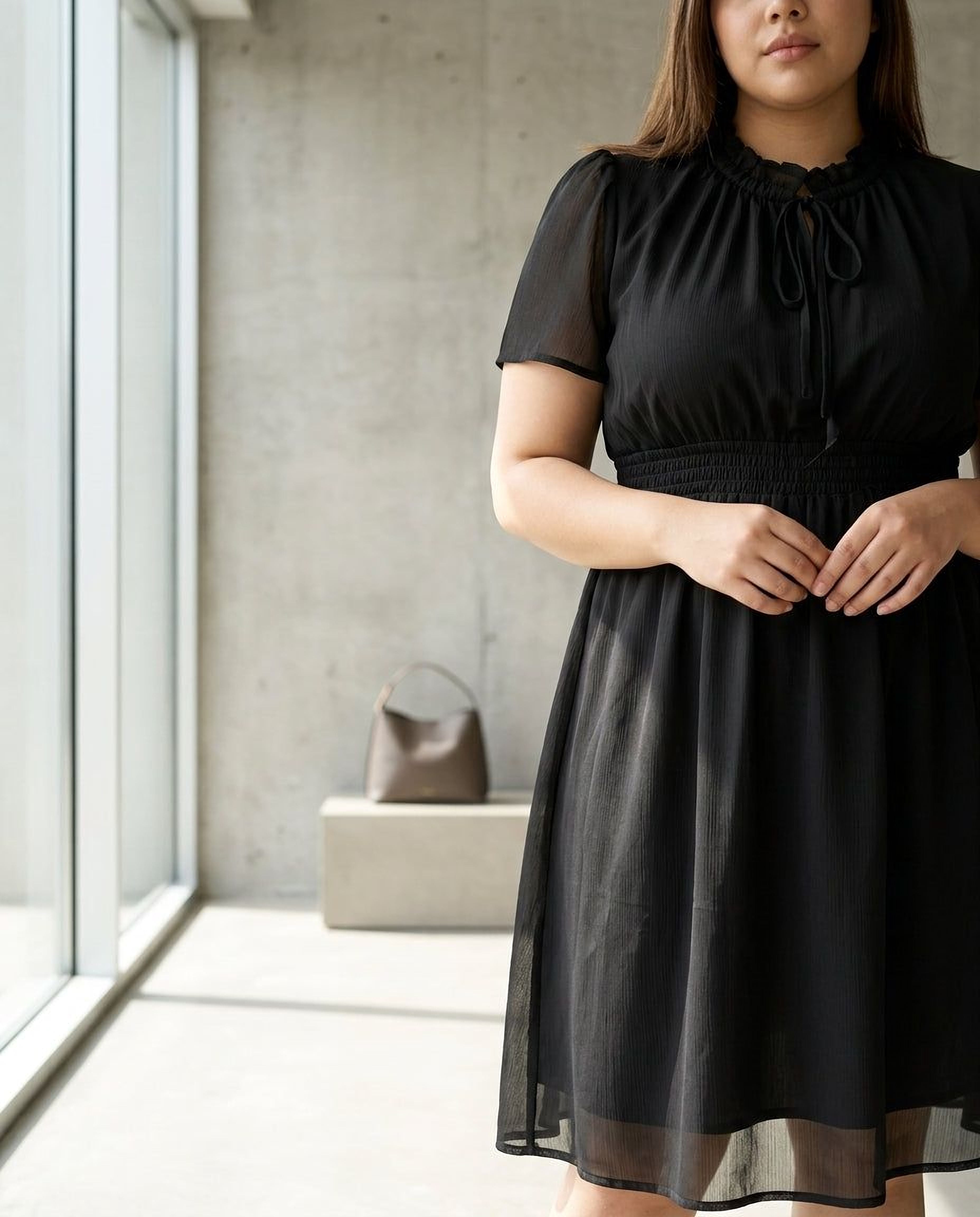 A woman wearing a black dress and high heels is smiling and looking down at her hand.