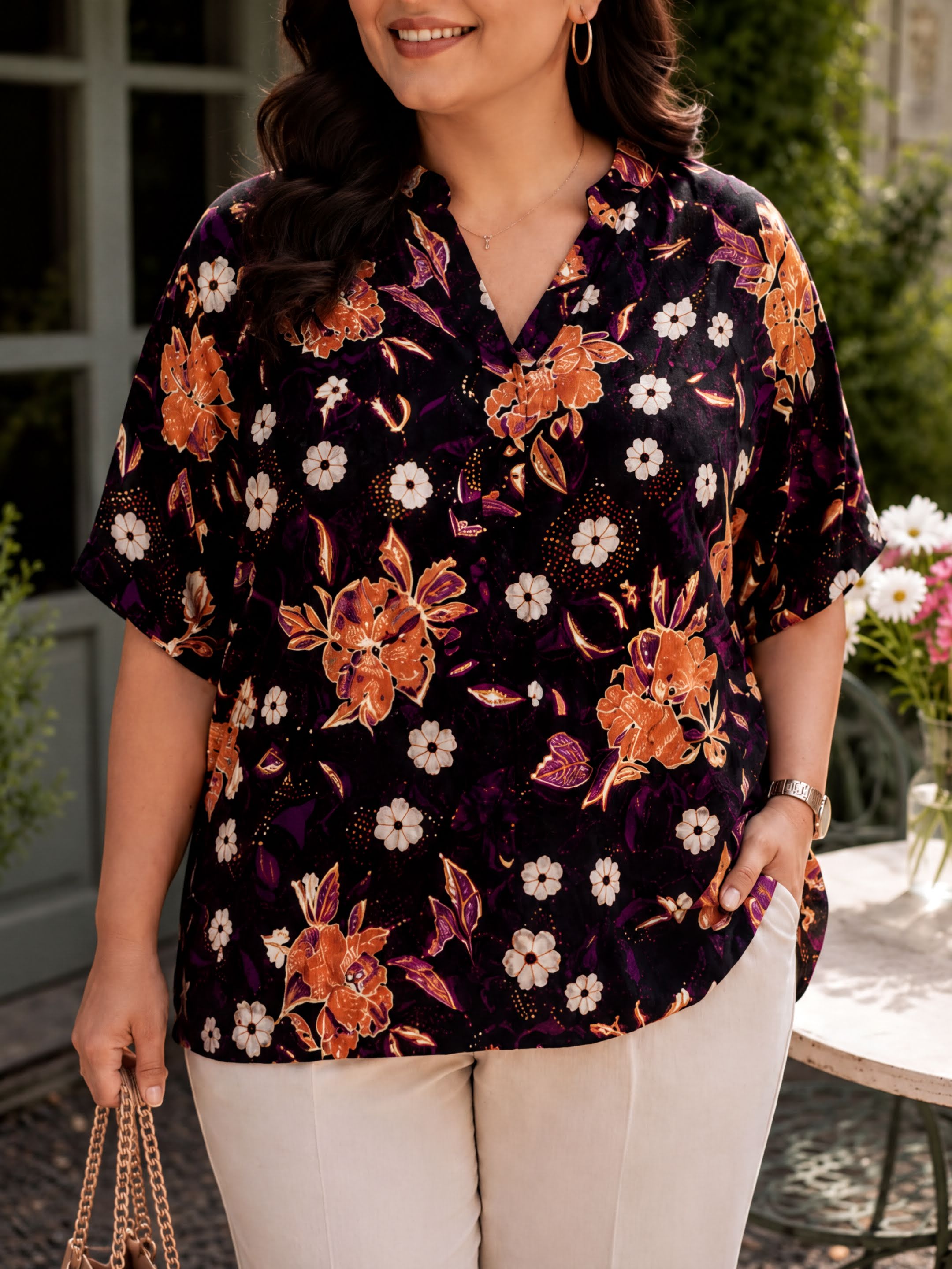 A woman wearing a floral print blouse stands outdoors, smiling and holding a purse.