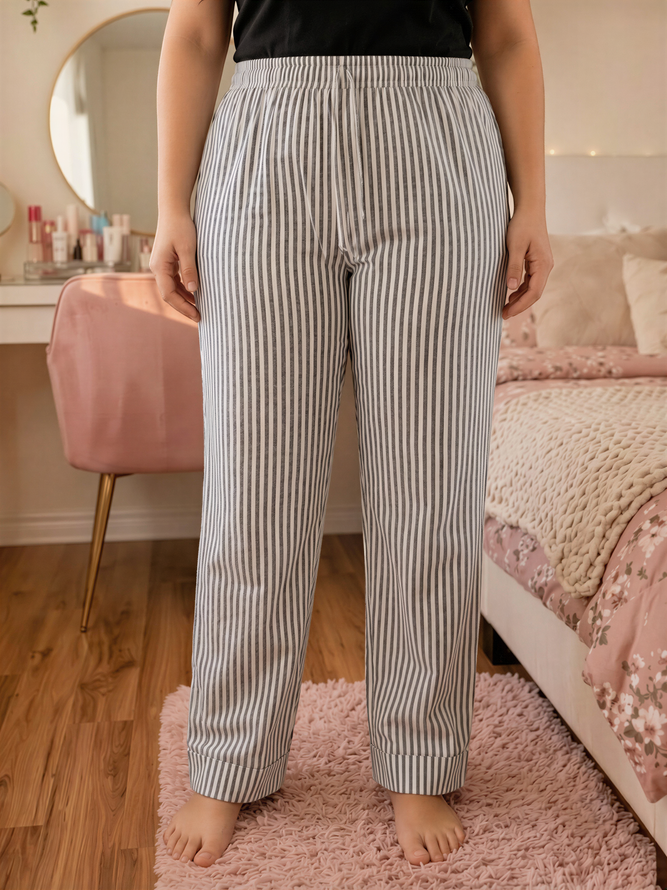 A person wearing striped pajama pants stands in a bedroom with a pink chair and a bed with a floral bedspread.