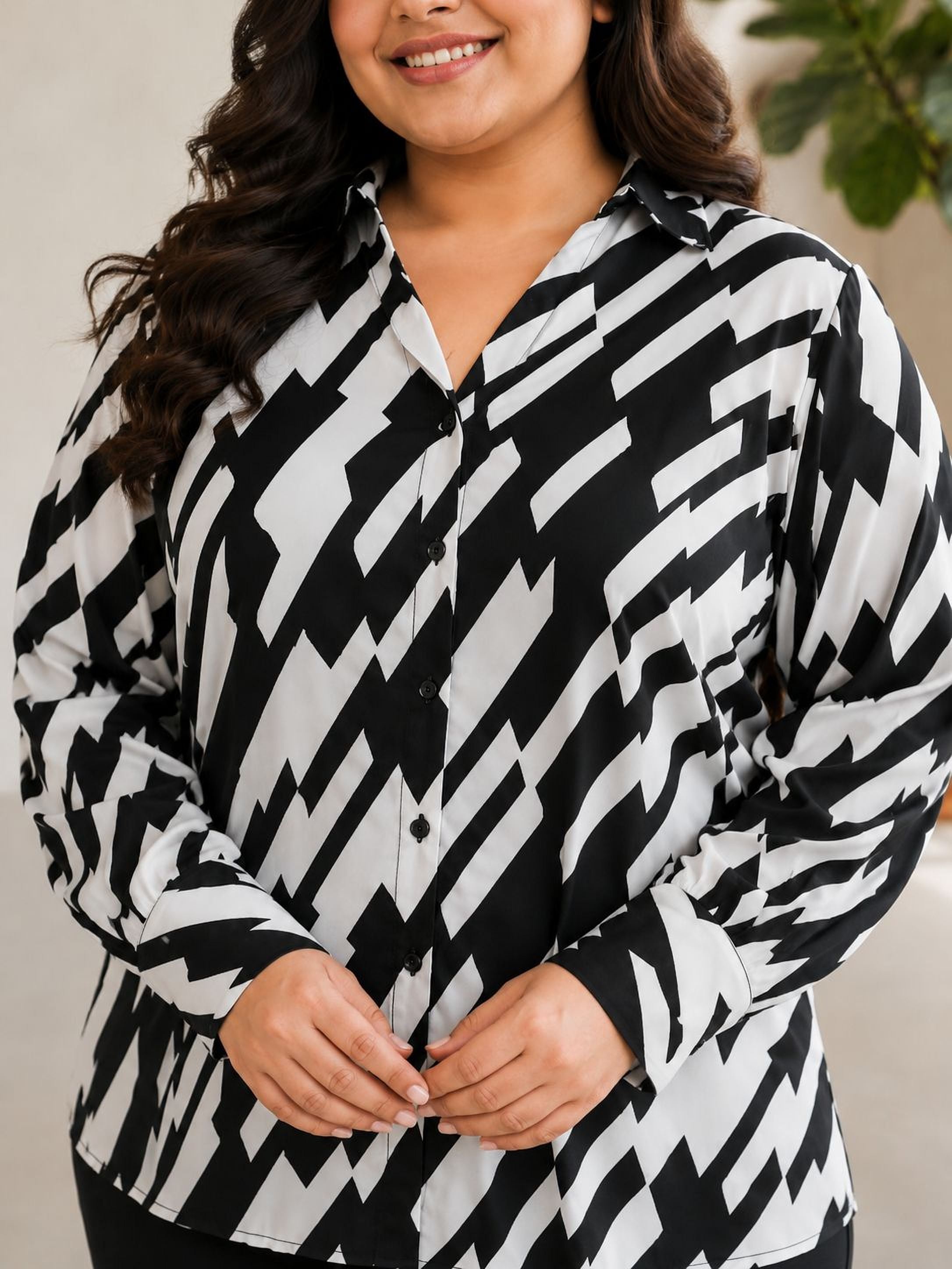A woman with long, dark hair is smiling and wearing a black and white patterned shirt.