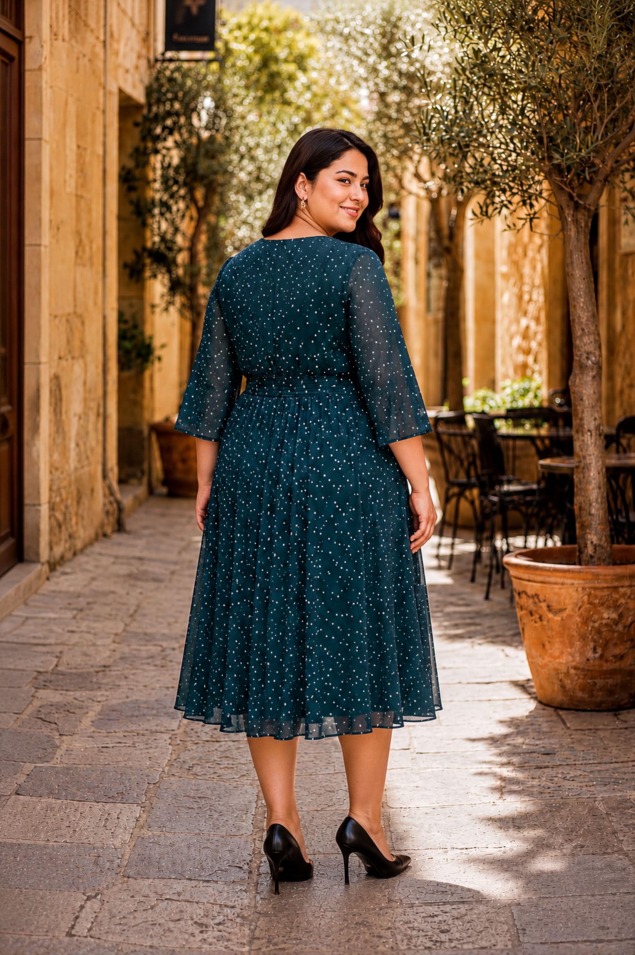 A woman wearing a green dress with white polka dots is walking down a stone-paved street, smiling at the camera.