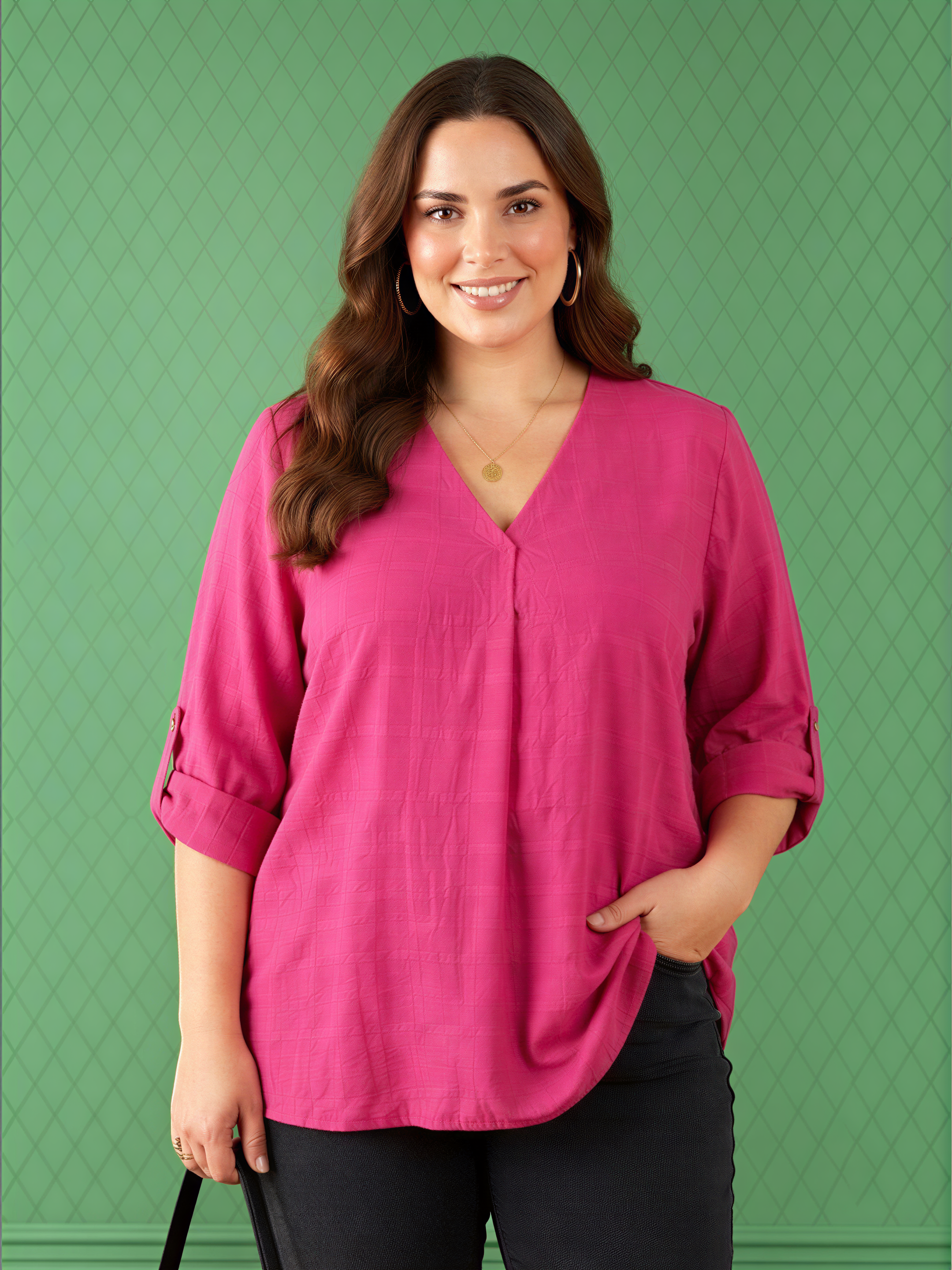 A woman with long brown hair is smiling and wearing a pink blouse against a green background.