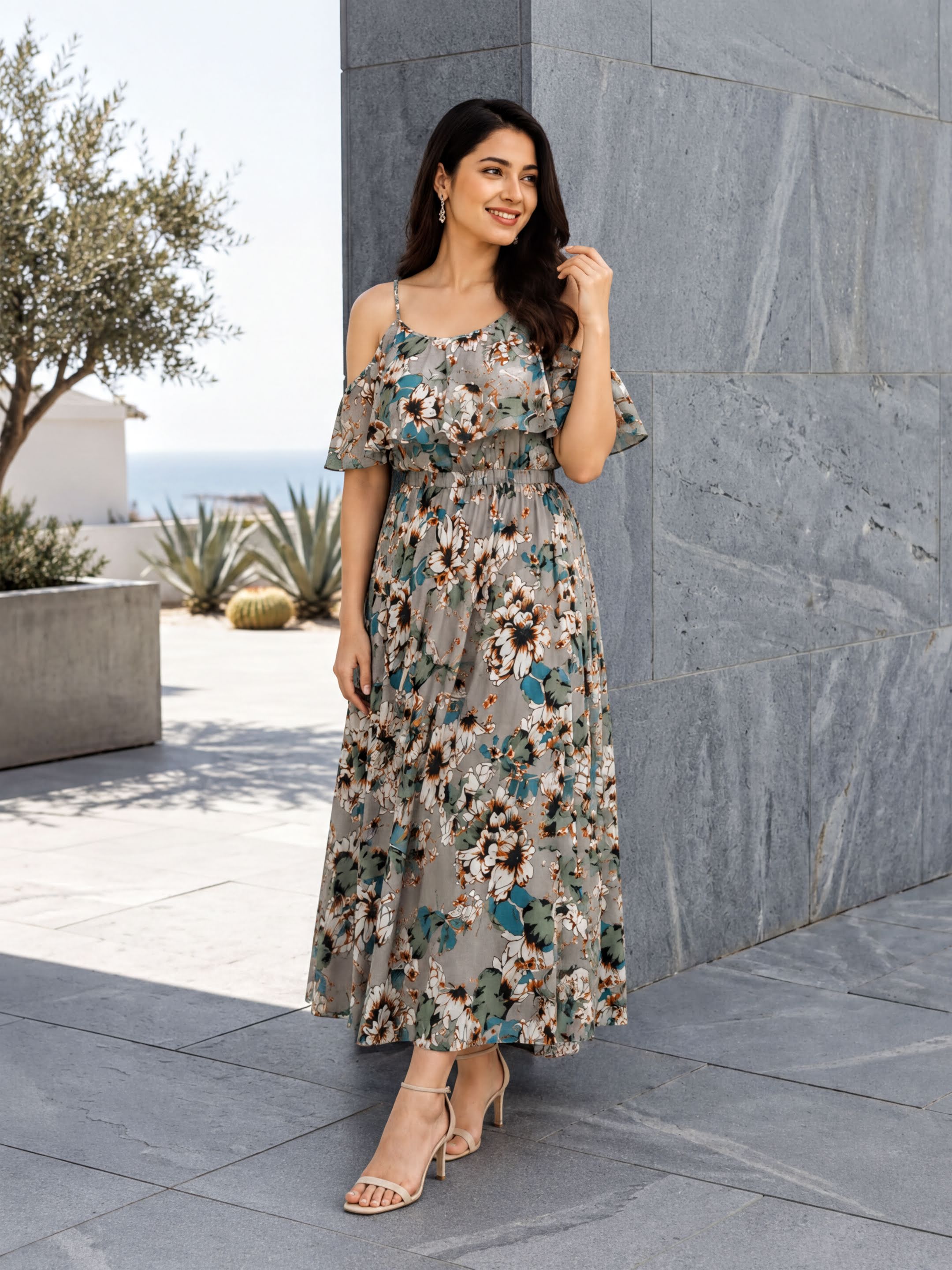 A woman wearing a floral print dress stands in front of a gray wall, smiling and looking to her left.