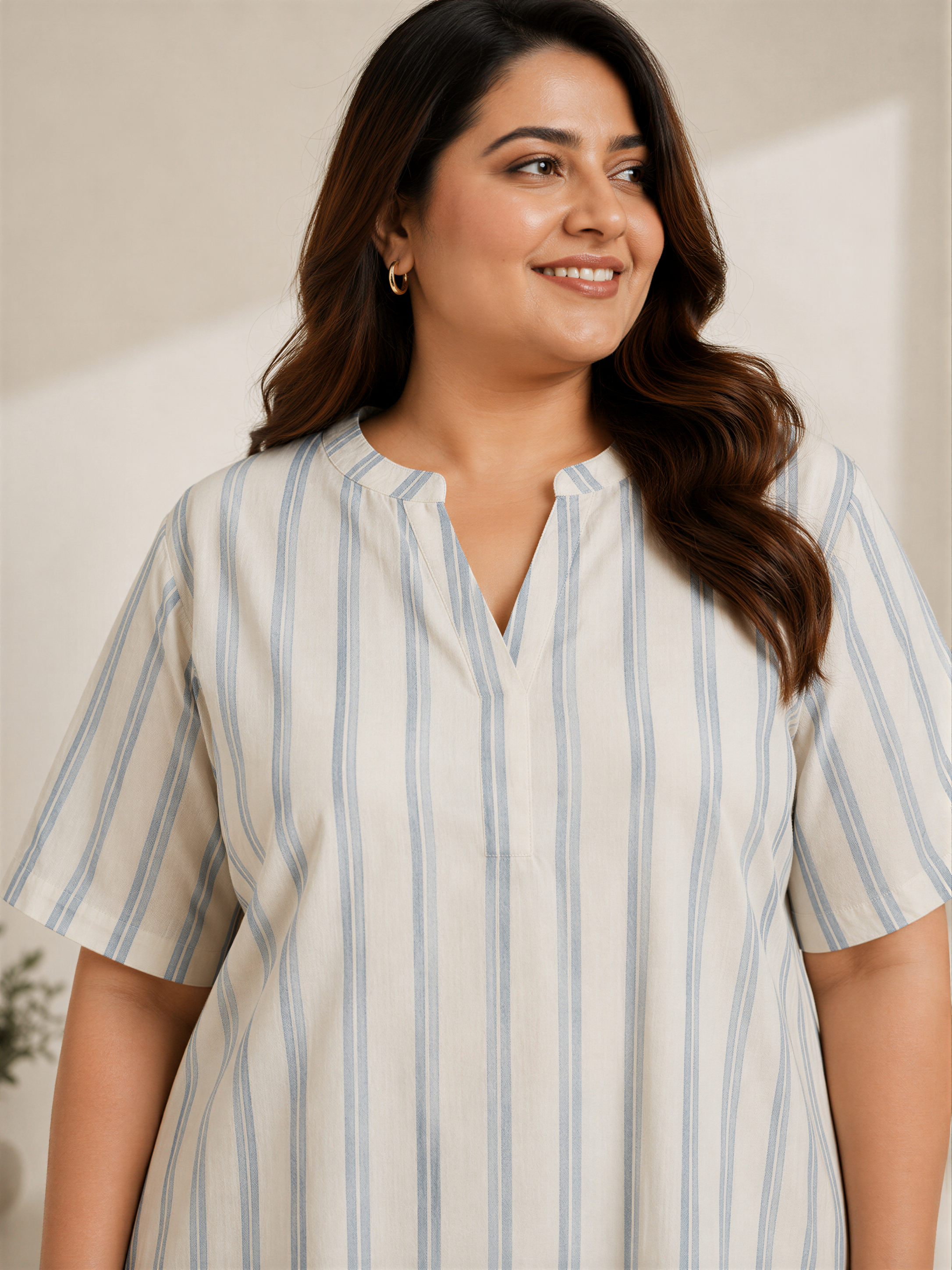 A woman with long brown hair wearing a striped dress is smiling and looking to the side.
