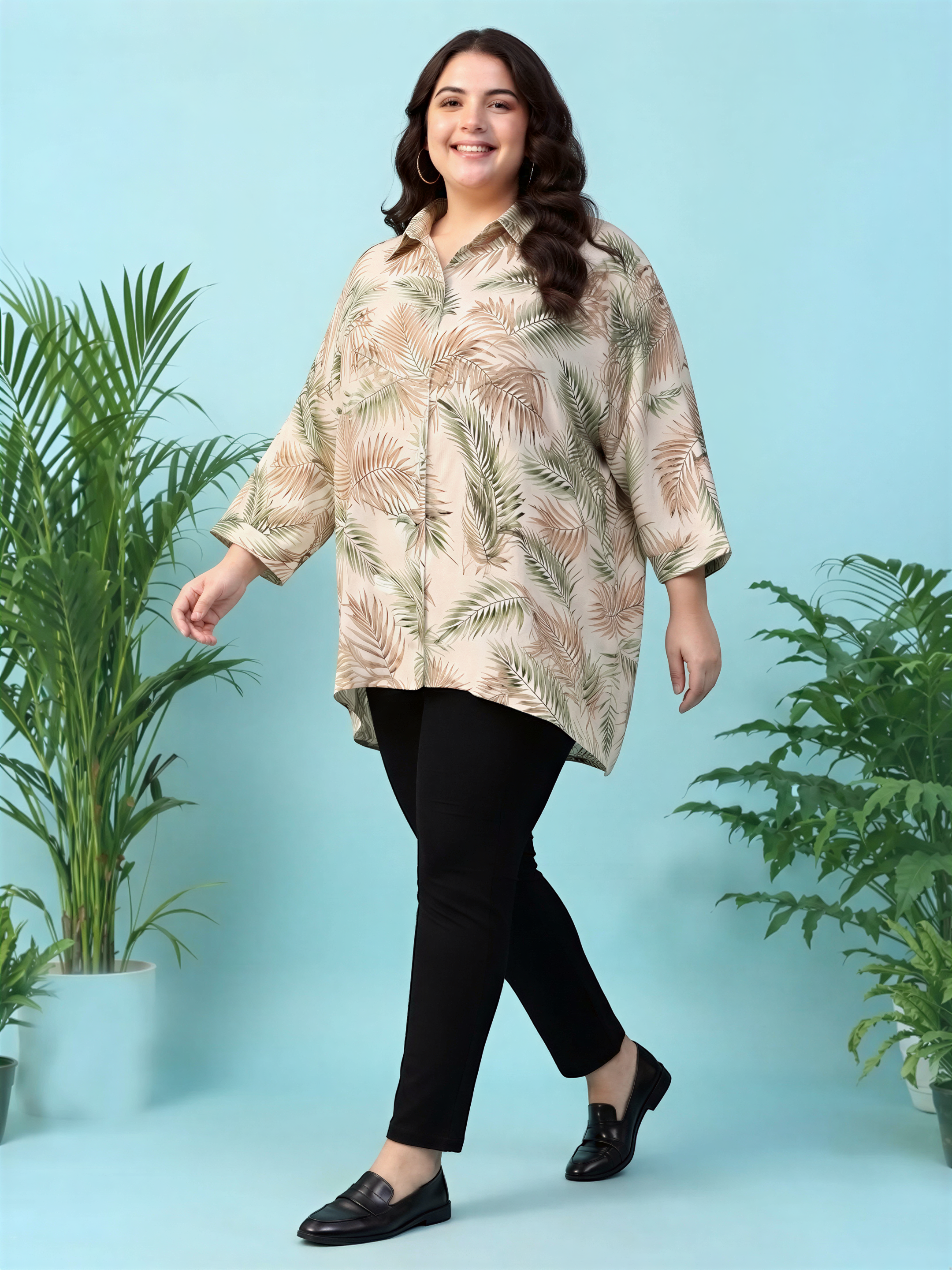 A woman wearing a floral print shirt and black pants is smiling and walking in front of two potted plants against a blue background.