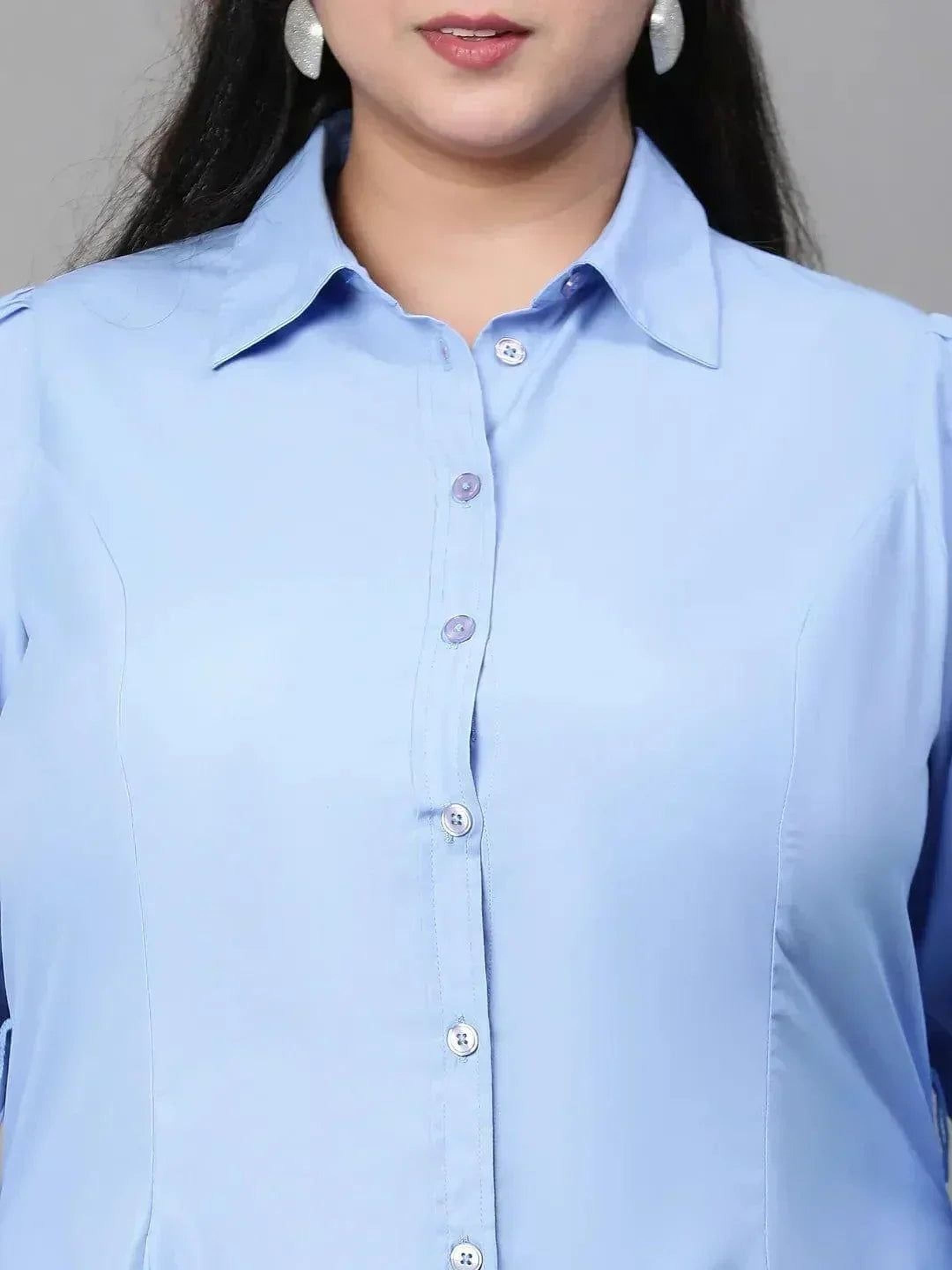A woman wearing a light blue dress and sunglasses stands confidently against a white background.