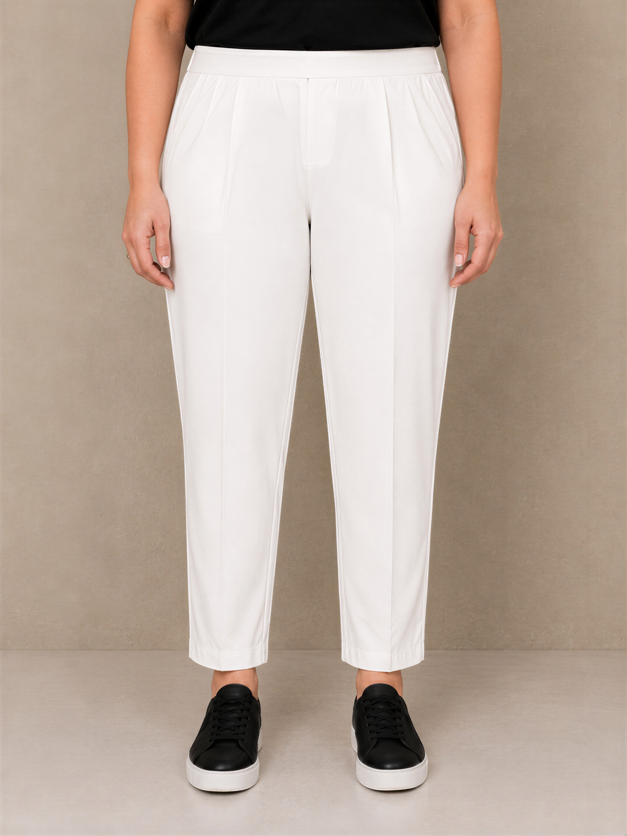 A person wearing white pants and black shoes stands against a beige background.